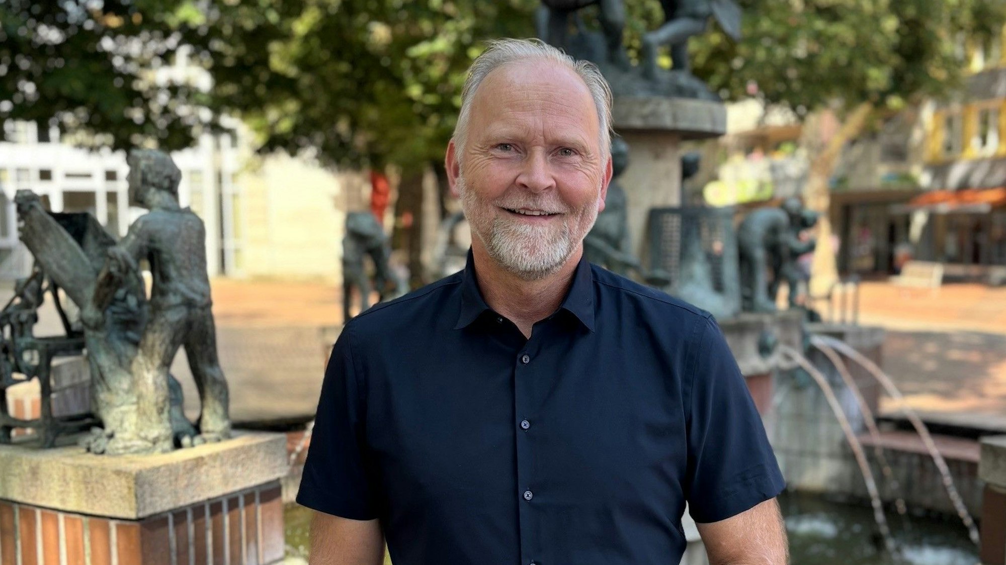Auf dem Bild ist der CDU Bürgermeisterkandidat vor einem Brunnen in der Fußgängerzone zu sehen.