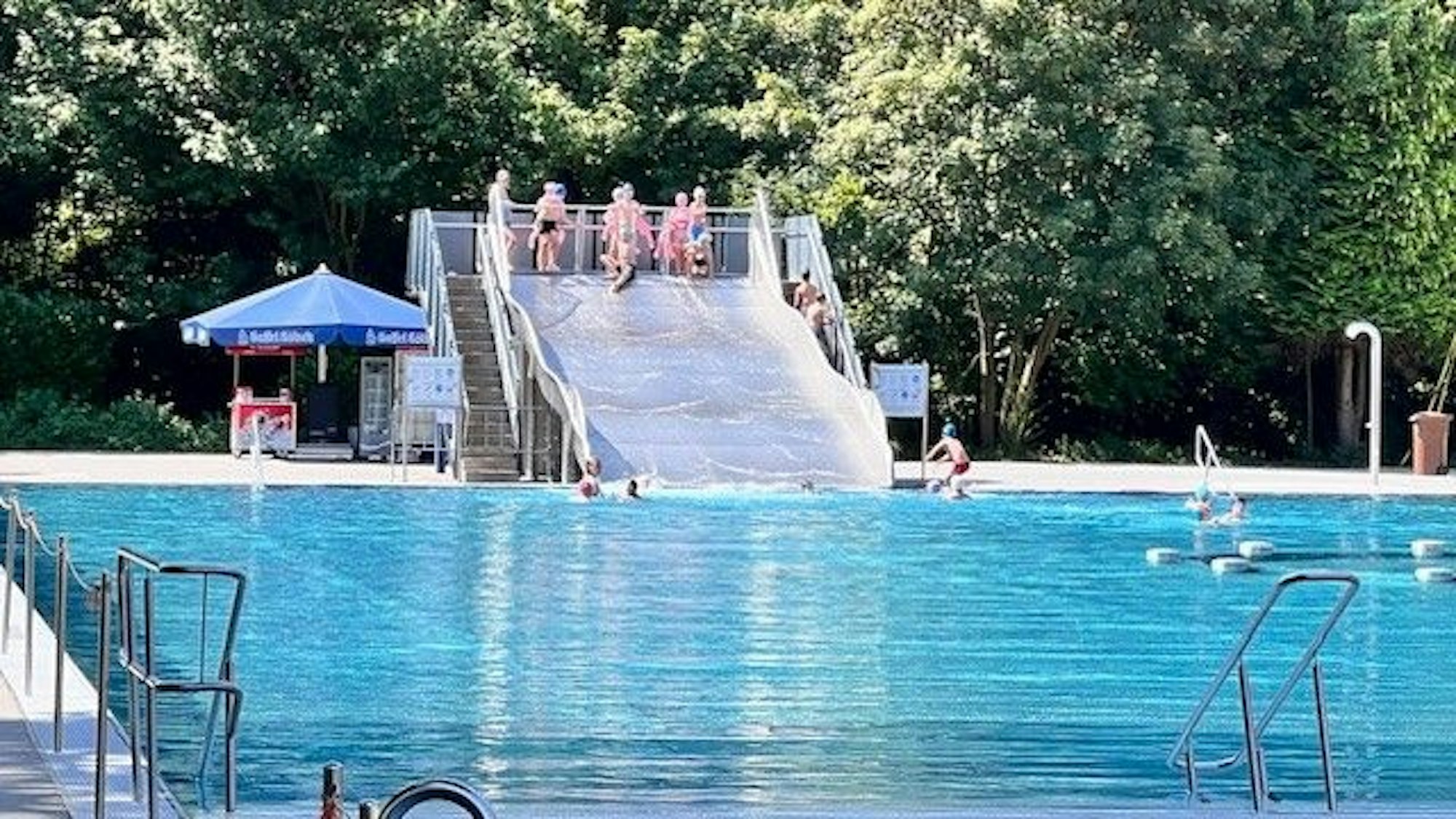Badegäste in einem Freibad rutschen über eine Wasserrutsche in ein Schwimmbecken.