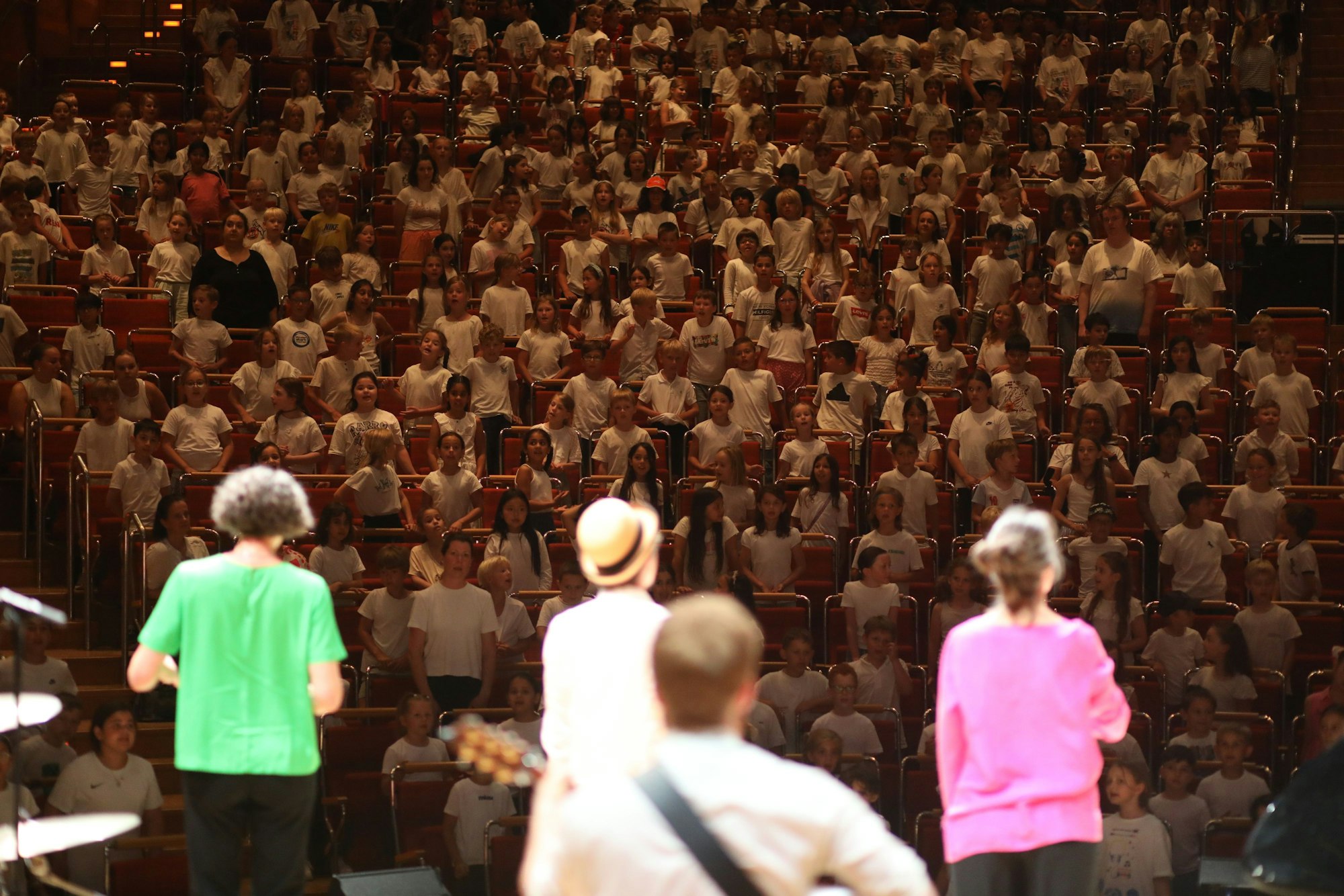 Vier bunt gekleidete Singleiterinnen und Singleiter stehen auf der Bühne der Kölner Philharmonie, die Besucherränge sind bis zum letzten Platz gefüllt mit Grundschulkindern.