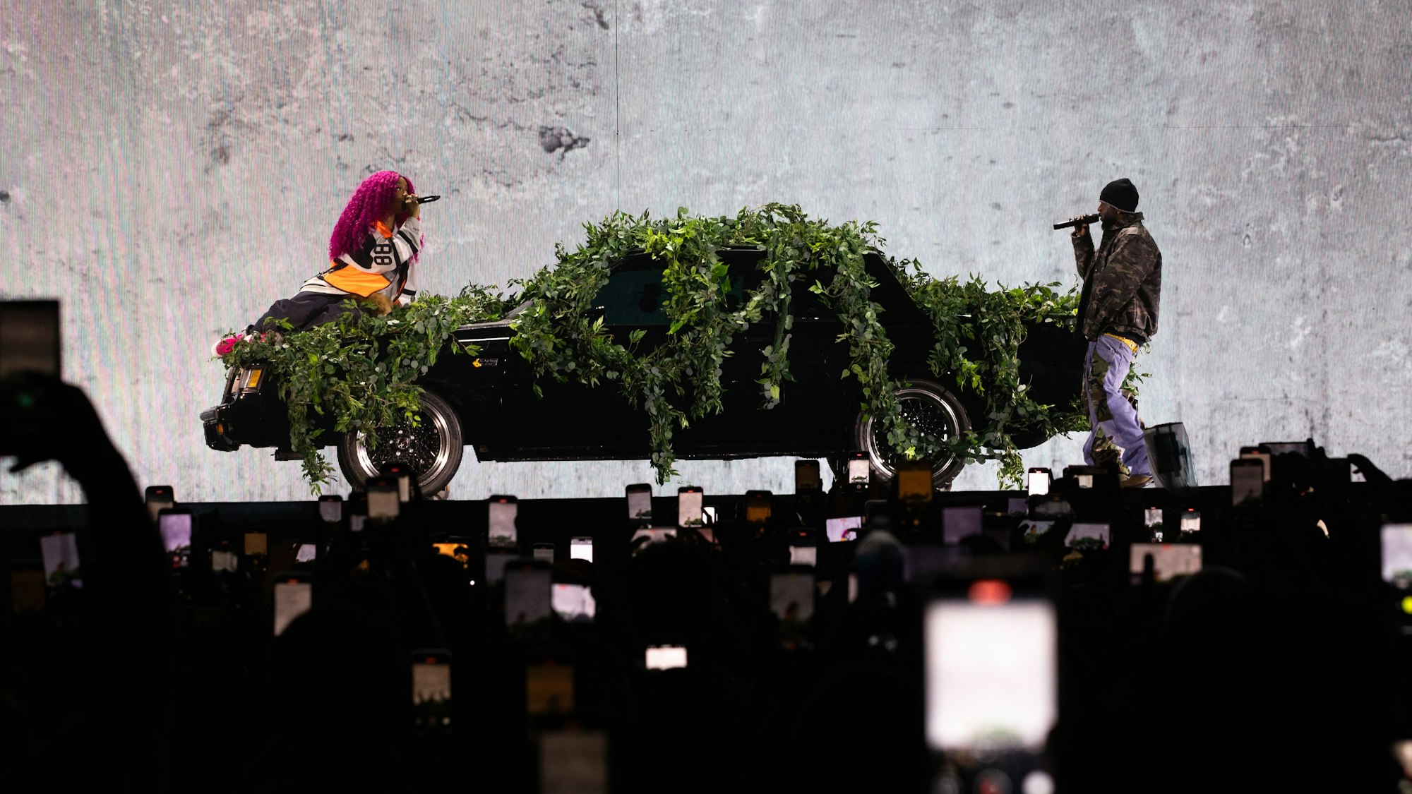 Vorne sieht man zahlreiche hochgehalten Handys. Dahinter lehnt SZA auf der Motorhaube des Buiks, Kendrick Lamar steht am Heck des Wagens.