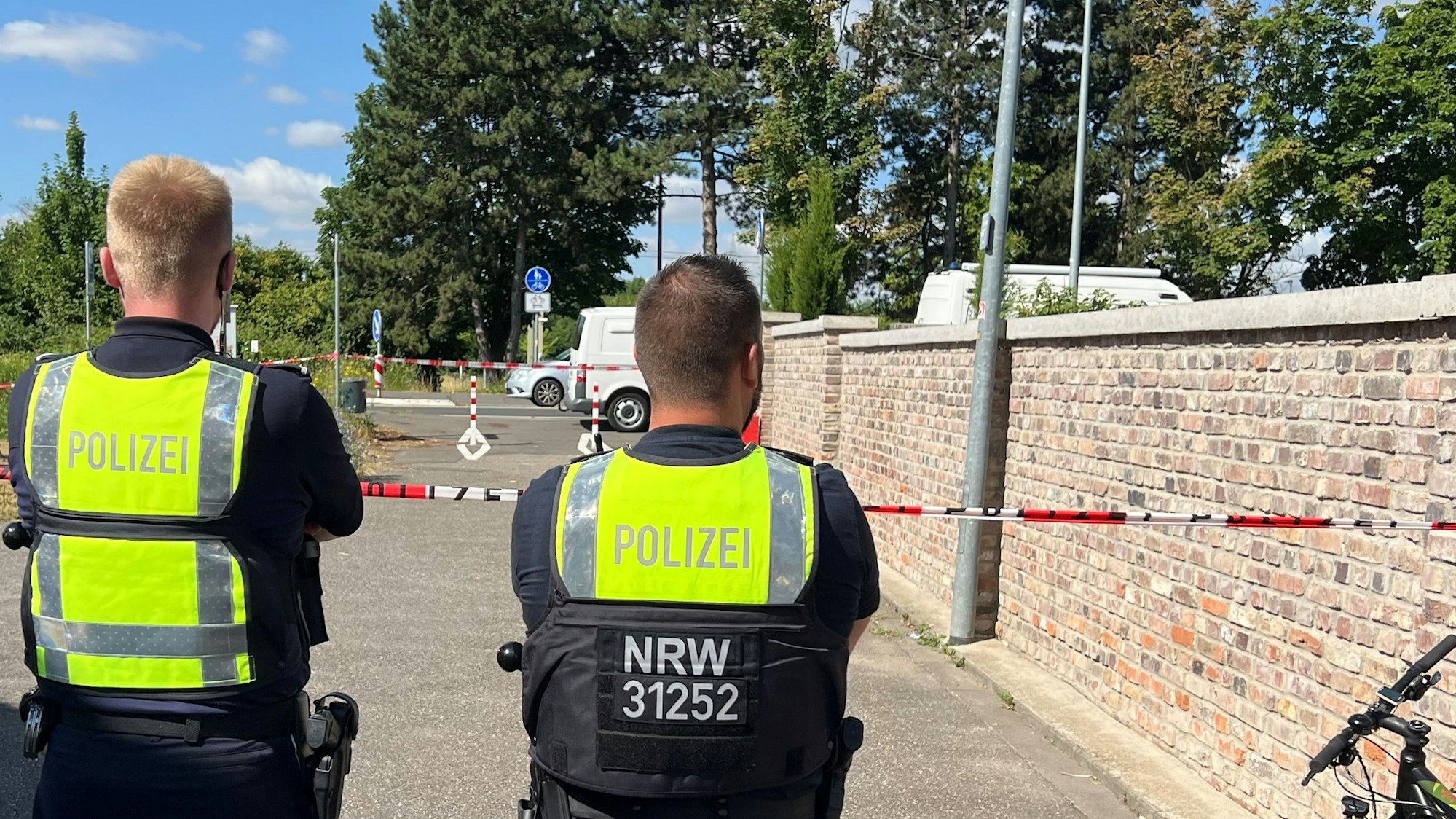 Das Bild zeigt zwei Polizeibeamte vor einer Absperrung.