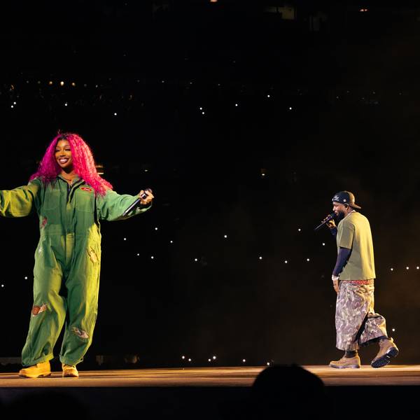 SZA steht links im grünen Overall auf dem Laufsteg im Stadioninnenraum, Kendrick Lamar rappt, von der Kamera abgewandt, rechts im Bild.