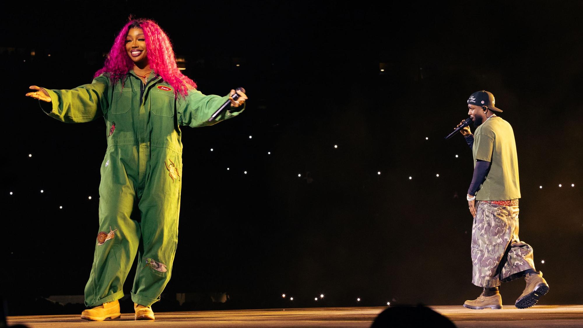 SZA steht links im grünen Overall auf dem Laufsteg im Stadioninnenraum, Kendrick Lamar rappt, von der Kamera abgewandt, rechts im Bild.