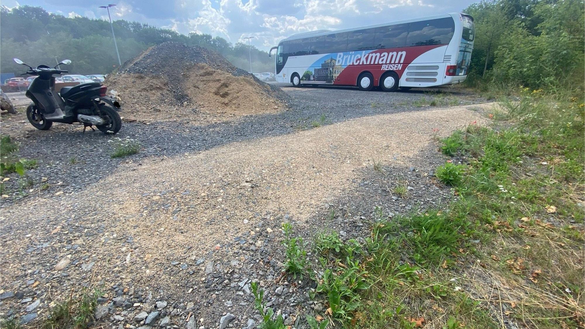 Zu sehen ist ein kleiner Wall aus Schotter und Sand, im Hintergrund steht ein Reisebus.
