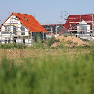 Neue Einfamilienhäuser, verkleidet mit Bauzaun, entstehen am Stadtrand.