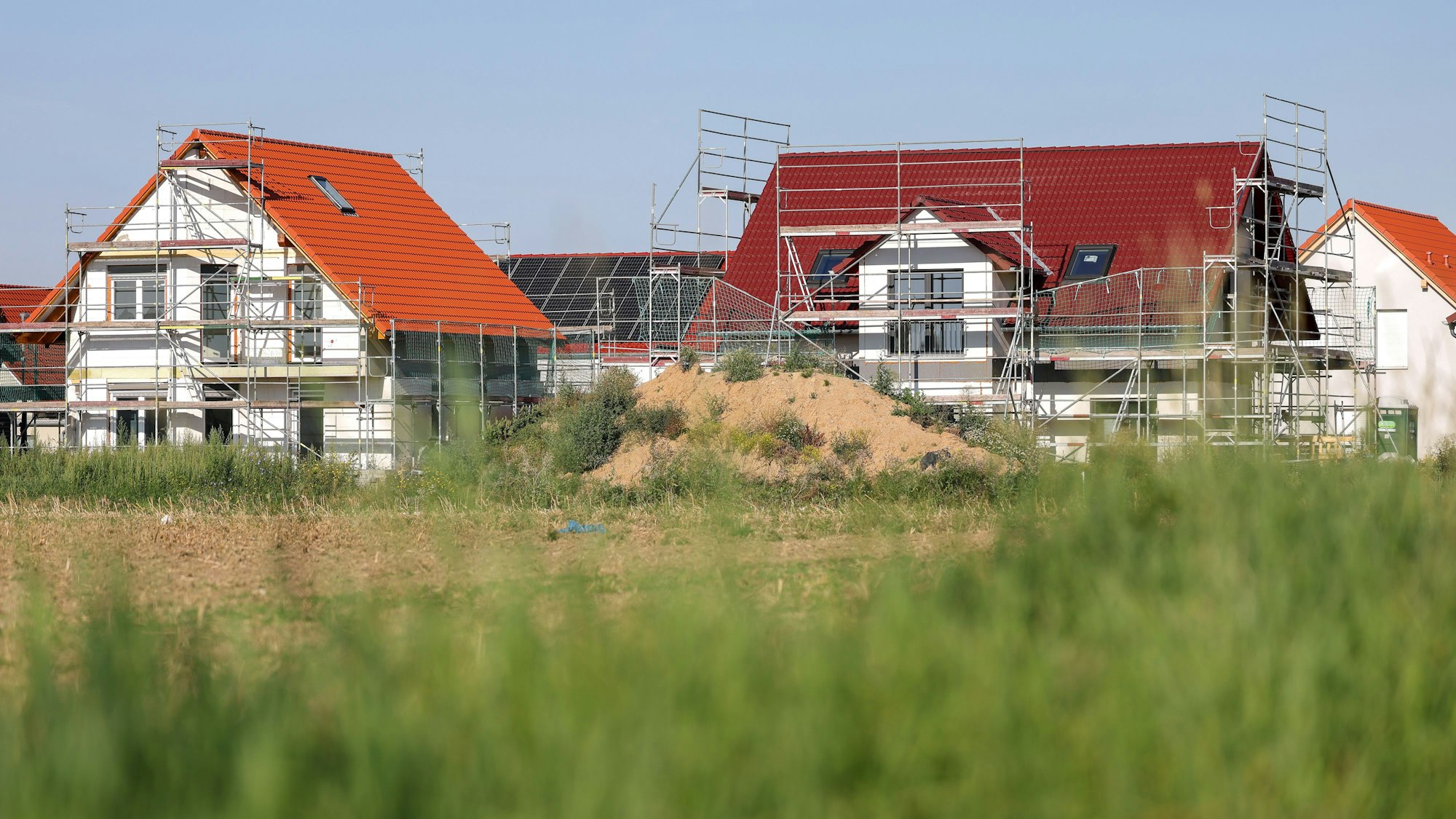 Neue Einfamilienhäuser, verkleidet mit Bauzaun, entstehen am Stadtrand.