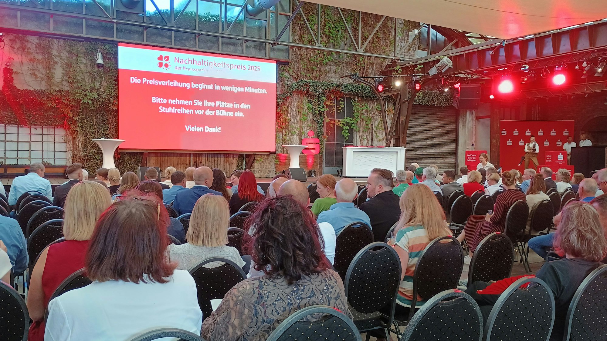 Zu sehen sind gut gefüllte Stuhlreihen vor der Bühne.