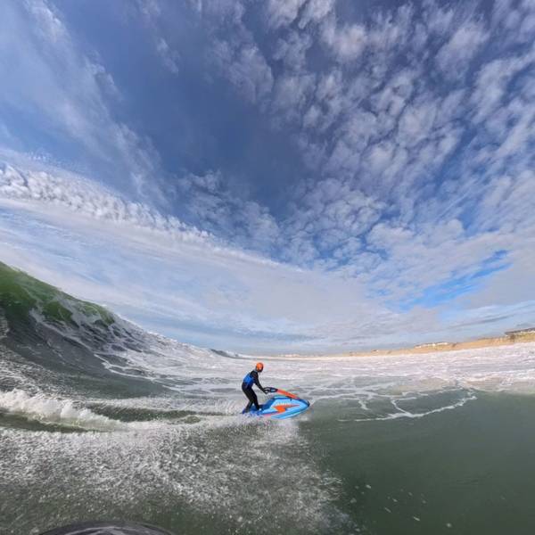 Zu sehen ist eine Jetski-Fahrerin mitten in einer riesigen Welle.