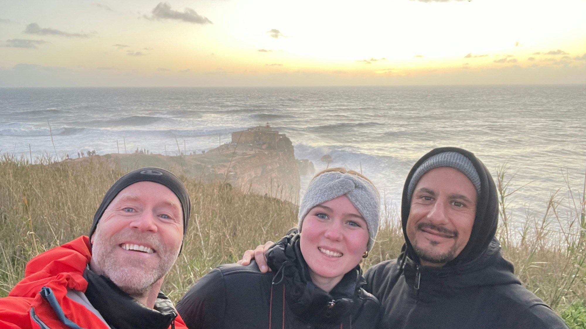 Drei Menschen machen ein Selfie, im Hintergrund ist die Atlantikküste Portugals zu sehen.