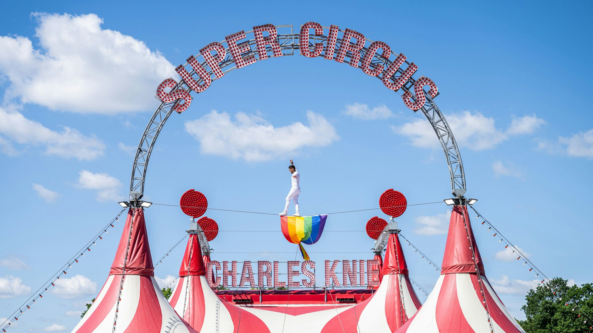 Der Hochseilartist David Ruiz vom Zirkus Charles Knie balanciert auf einem Seil über dem Zirkuszelt, wo eine Regenbogenfahne aus Protest hängt.