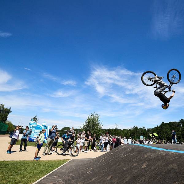Lennox Zimmermann macht mit seinem BMX-Bike einen Salto in der Luft, am Boden steht eine Schar Zuschauer.
