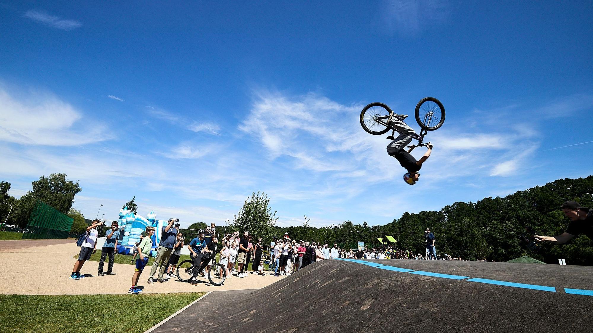 Lennox Zimmermann macht mit seinem BMX-Bike einen Salto in der Luft, am Boden steht eine Schar Zuschauer.