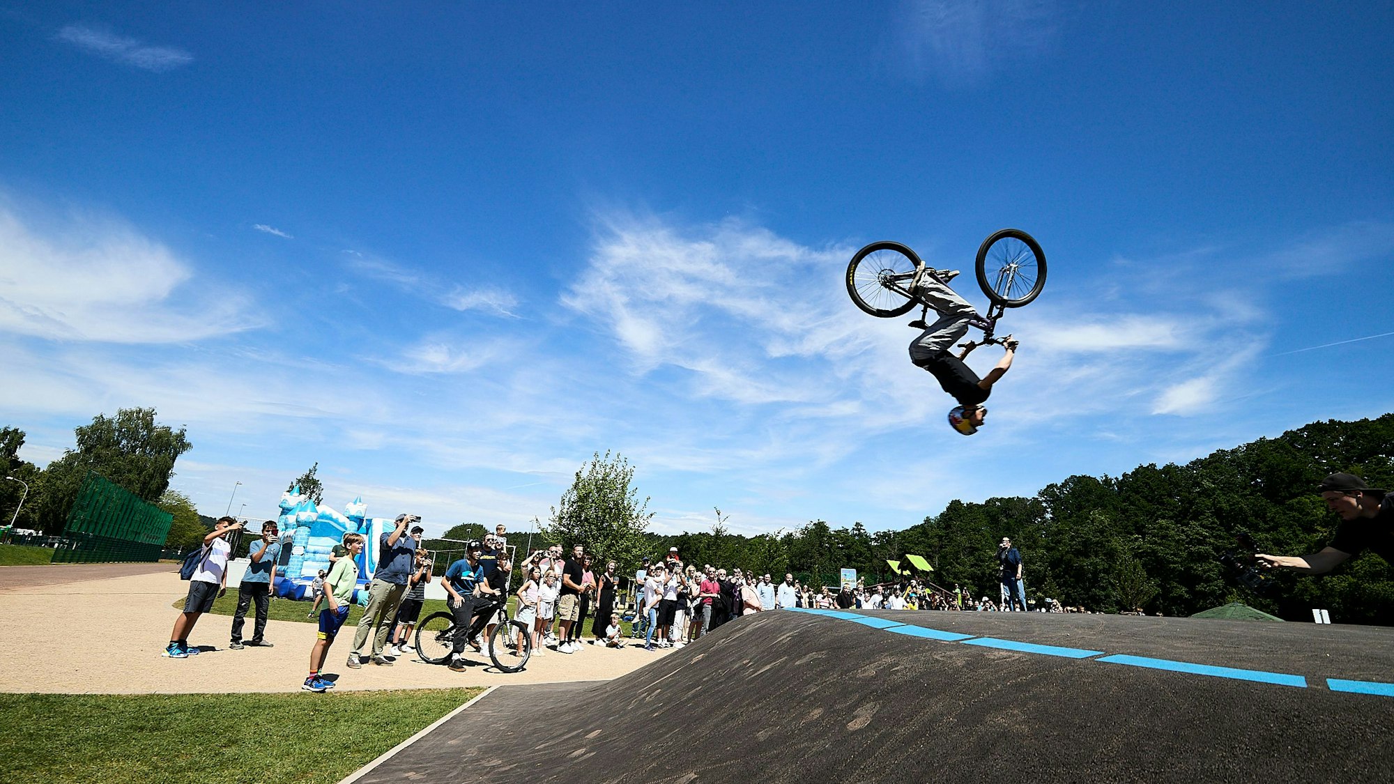 Lennox Zimmermann macht mit seinem BMX-Bike einen Salto in der Luft, am Boden steht eine Schar Zuschauer.