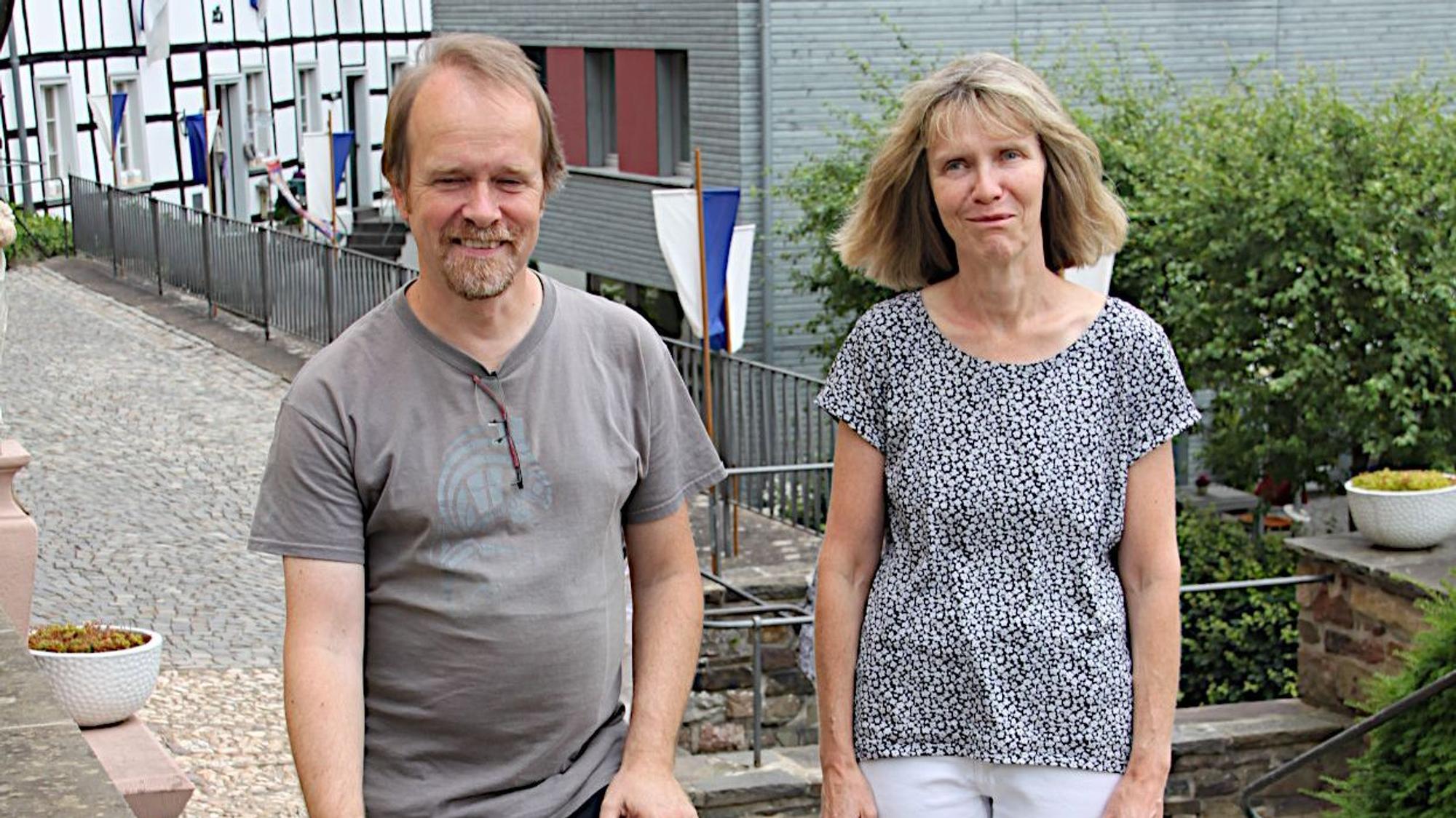 Ein Mann und eine Frau stehen nebeneinander, im Hintergrund ist ein mit Fahnen geschmücktes Fachwerkhaus zu sehen.