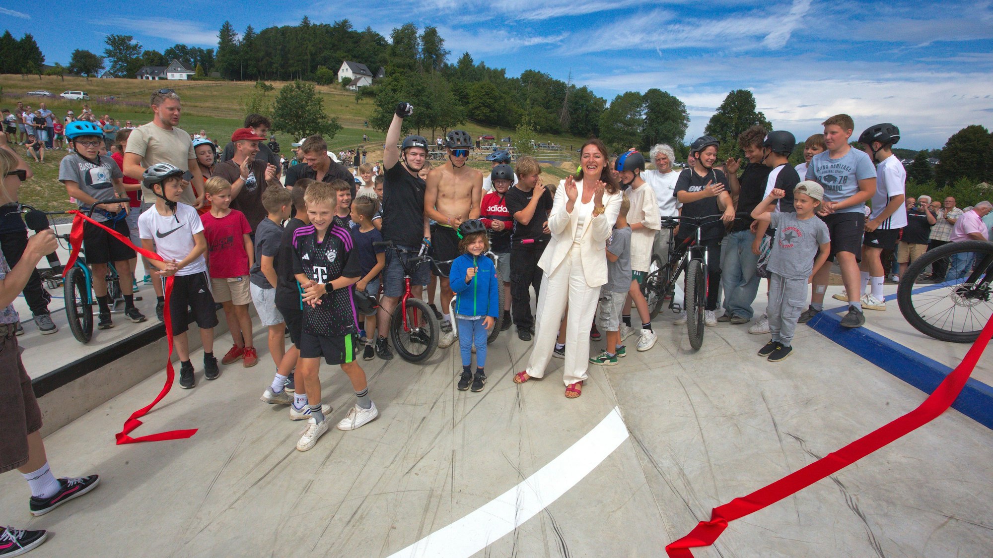 Zur Eröffnung des Skate- und Bikeparks in der Ortschaft Niederhof durchschnitt Waldbröls Bürgermeisterin Larissa Weber (in weiß) ein rotes Band.