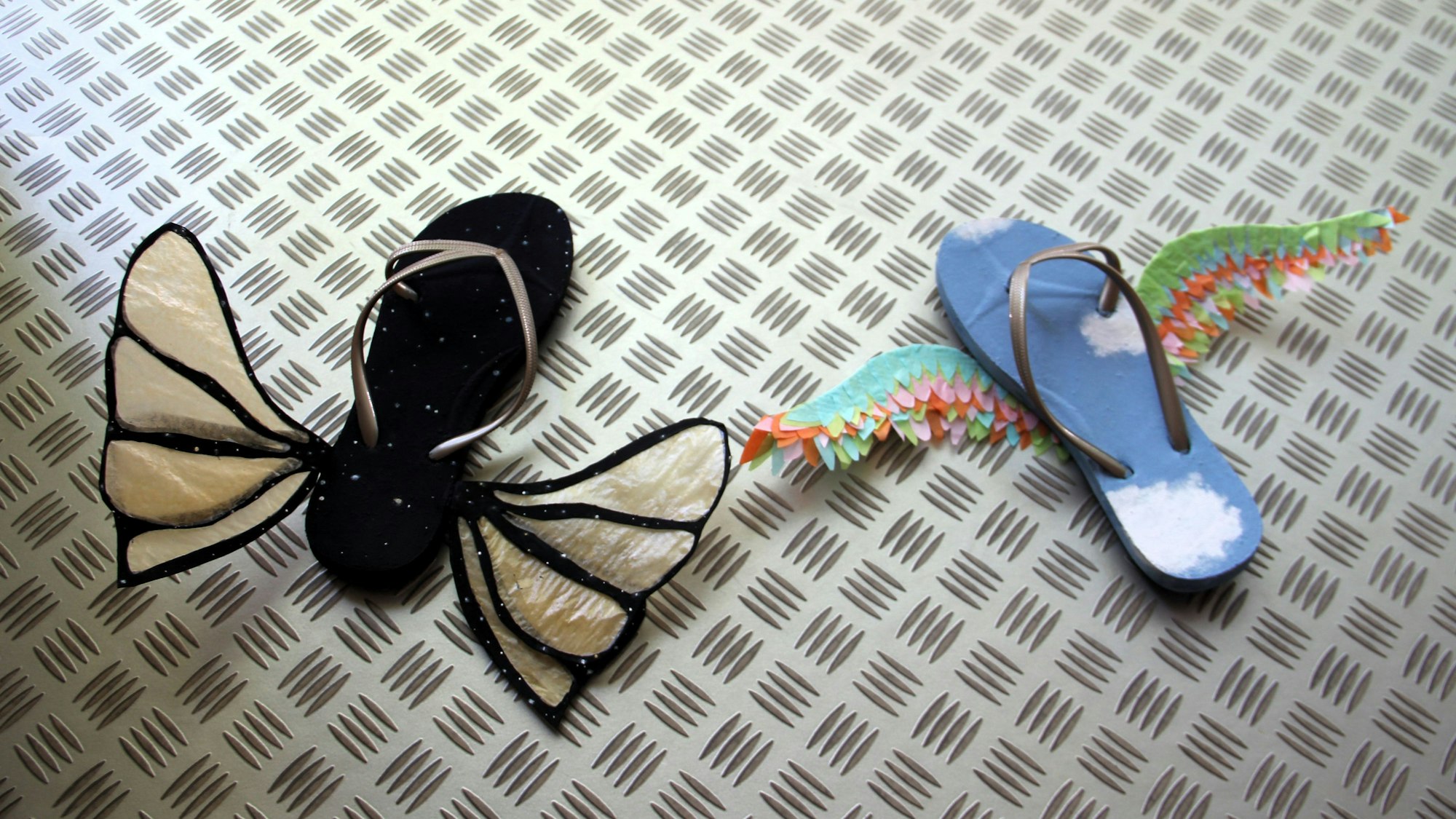 Auf einer Stahlplatte liegen Flip-Flops, an die Flügel angebracht wurden.