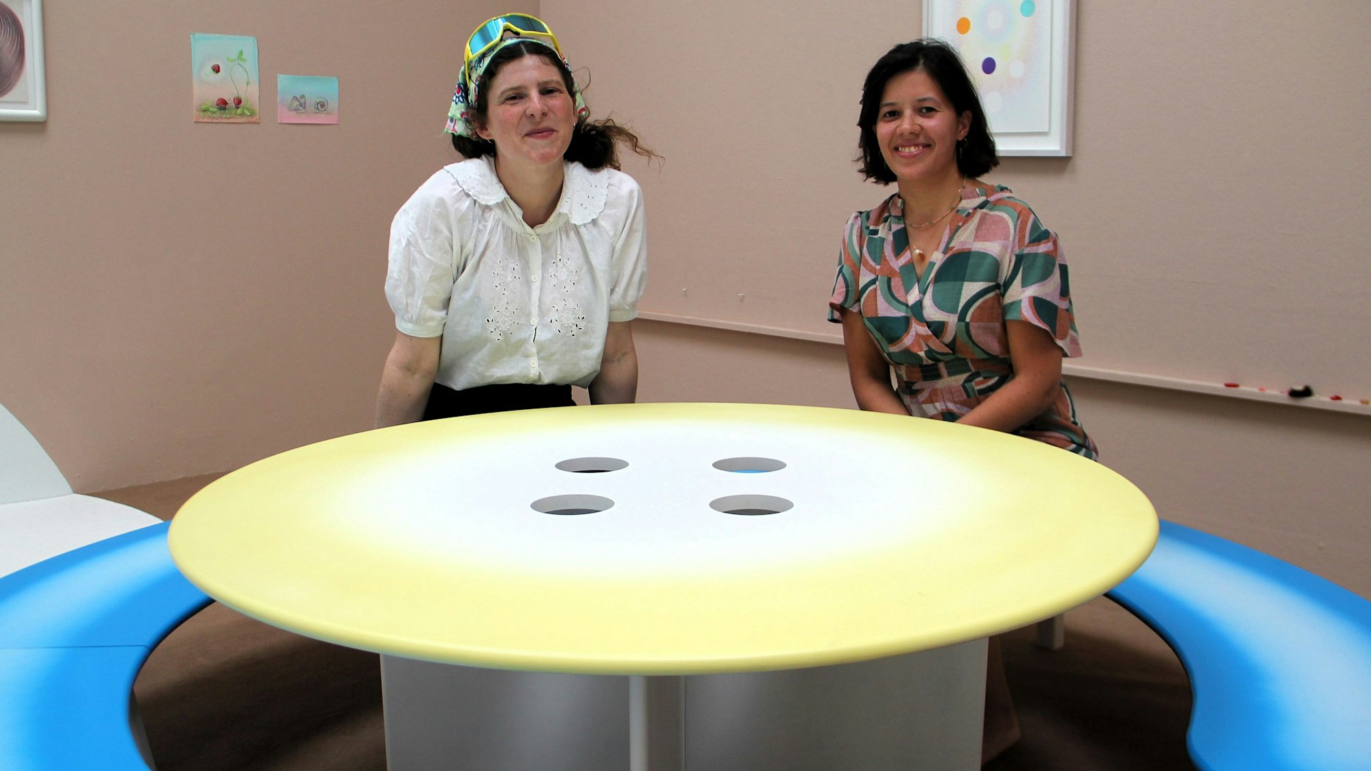 Zwei junge Frauen sitzen an einem runden Tisch, der vier Löcher hat.