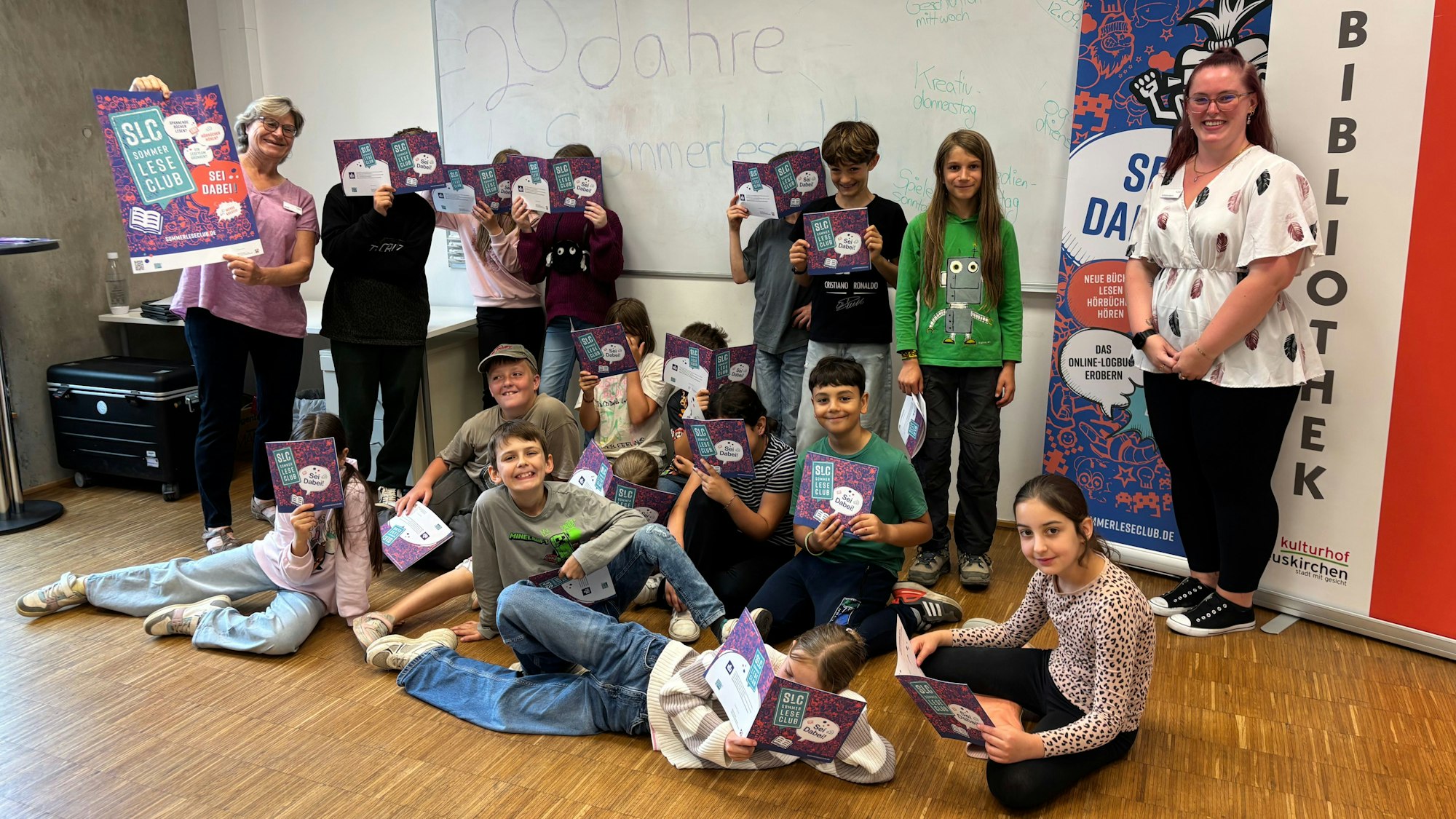 Kinder lesen in unterschiedlichen Posen in Flyern. Die Gruppe wird von zwei Frauen flankiert.
