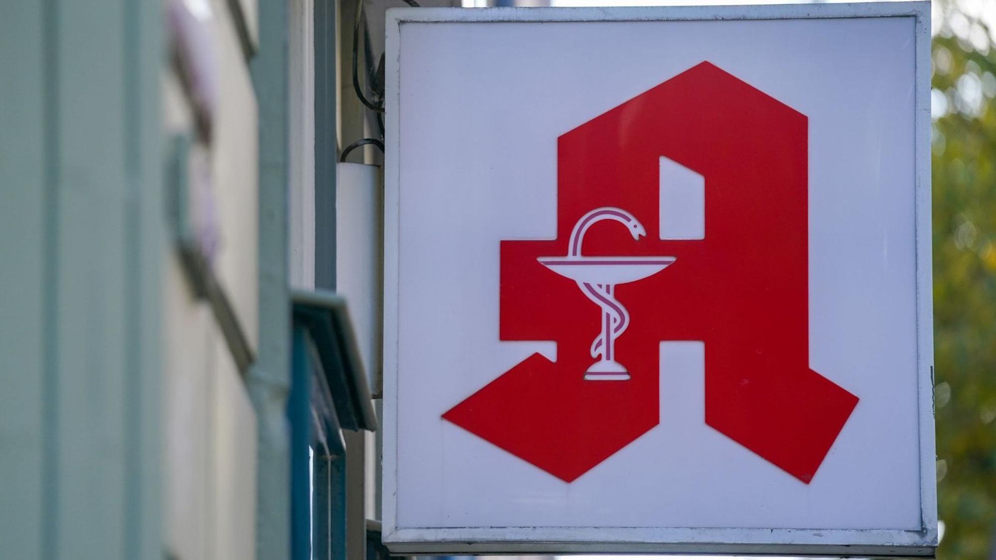 Ein Apotheken-Logo hängt an der Eingangsfassade einer Apotheke.