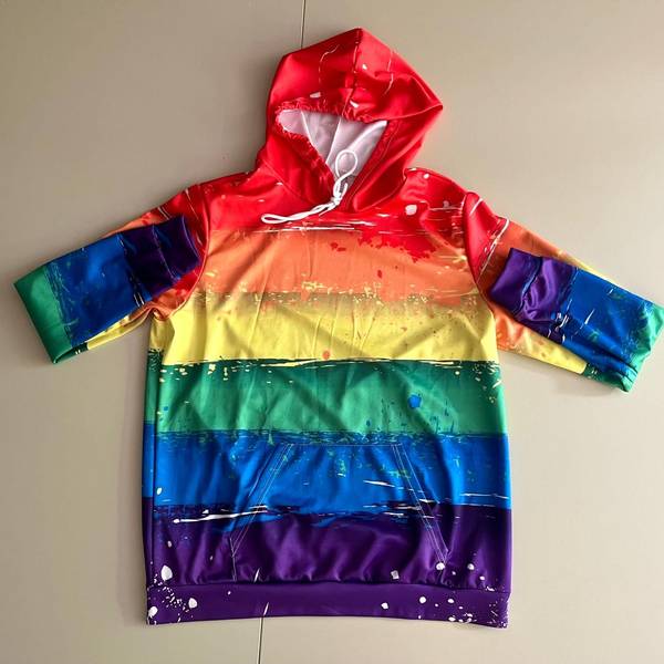 Ein Kapuzenpullover in Regenbogenfarben liegt ausgebreitet auf einem neutralen Hintergrund