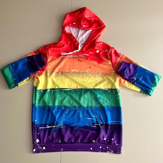 Ein Kapuzenpullover in Regenbogenfarben liegt ausgebreitet auf einem neutralen Hintergrund