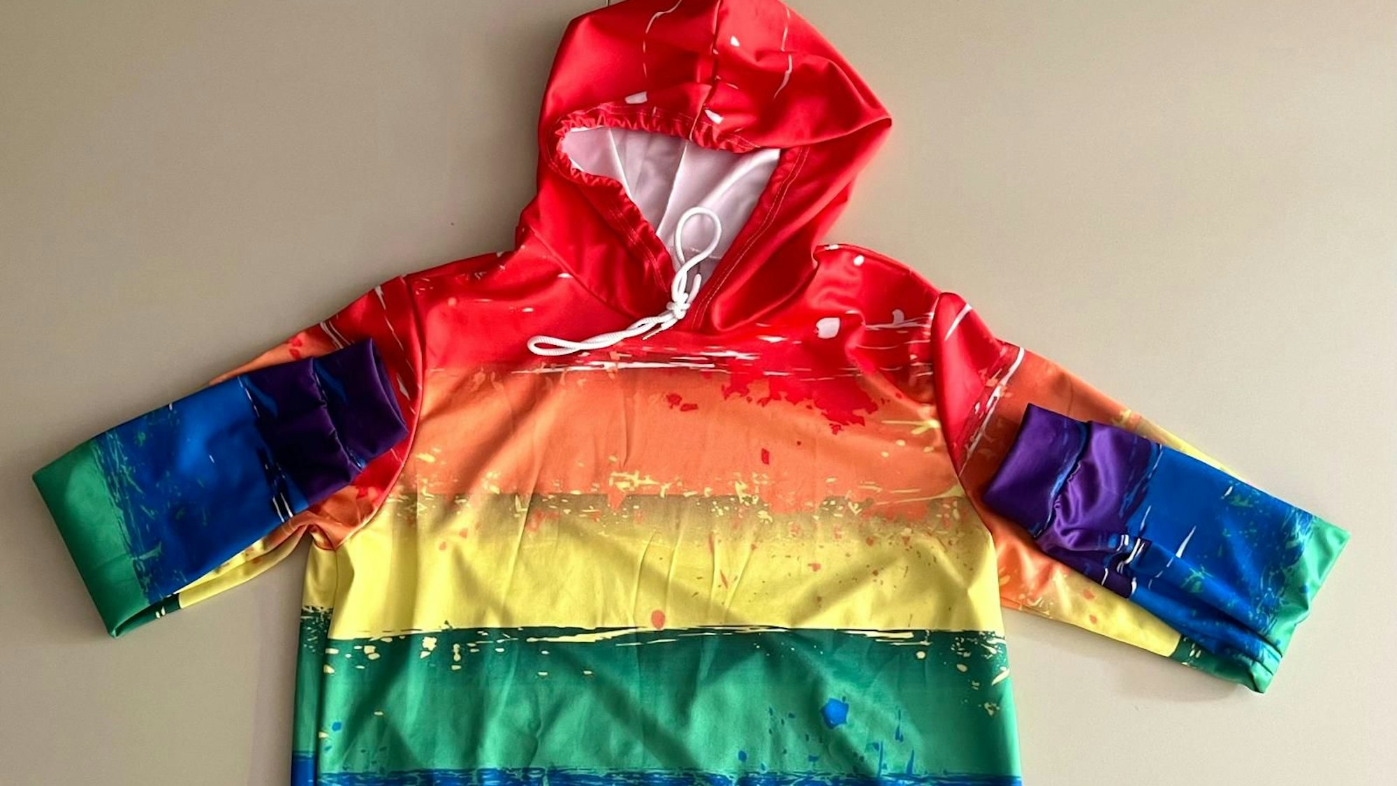 Ein Kapuzenpullover in Regenbogenfarben liegt ausgebreitet auf einem neutralen Hintergrund