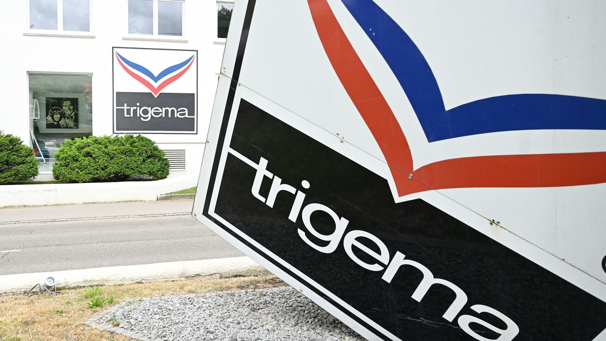 Ein Logo der Bekleidungsfirma Trigema ist am Gebäude des Firmensitzes angebracht, links ein Foto von Ex-Trigema-Chef Wolfgang Grupp.