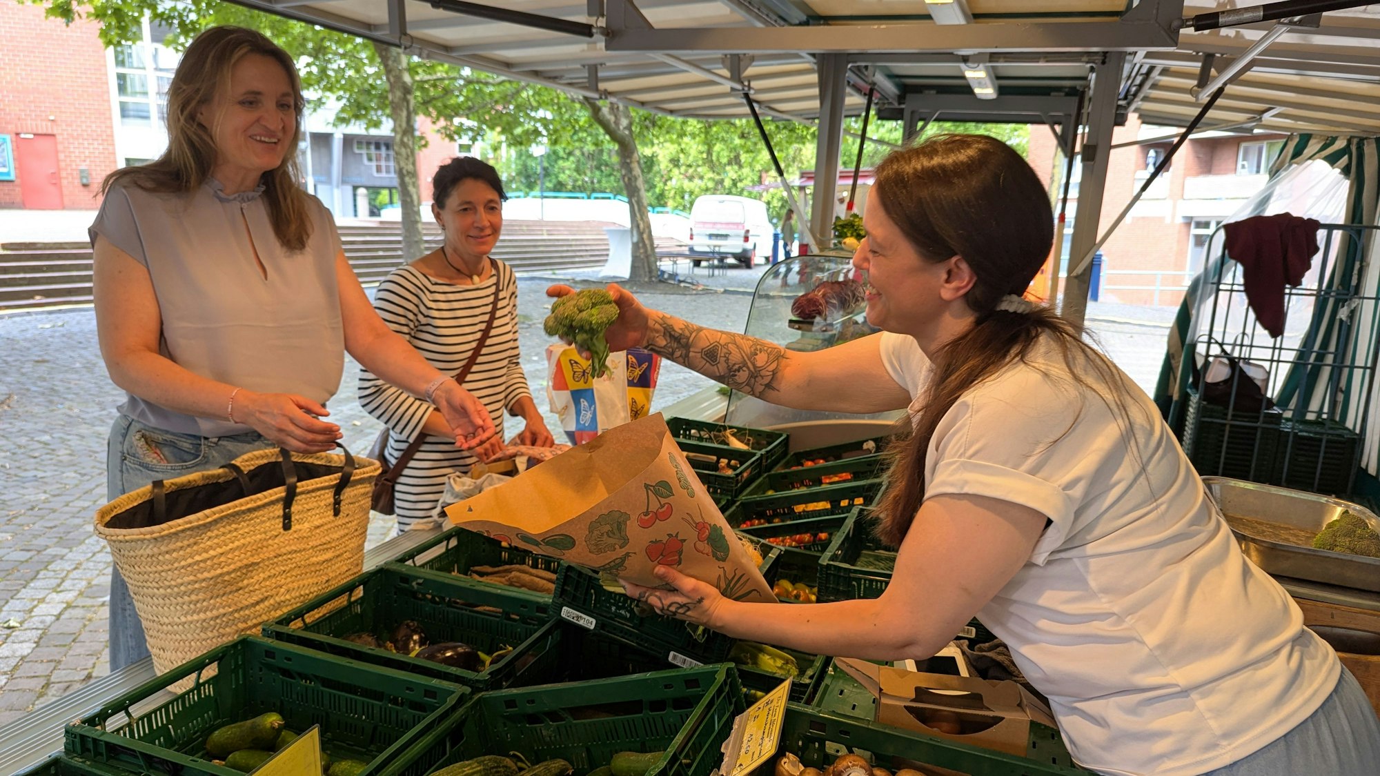 Das Foto zeigt eine Markthändlerin und Kunden am Obst- und Gemüsestand auf dem Wochenmarkt in Hürth.