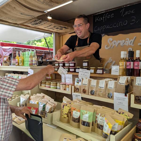 Das Foto zeigt den Marktmeister und einen Händler an seinem Pralinen-Stand auf dem Hürther Wochenmarkt.