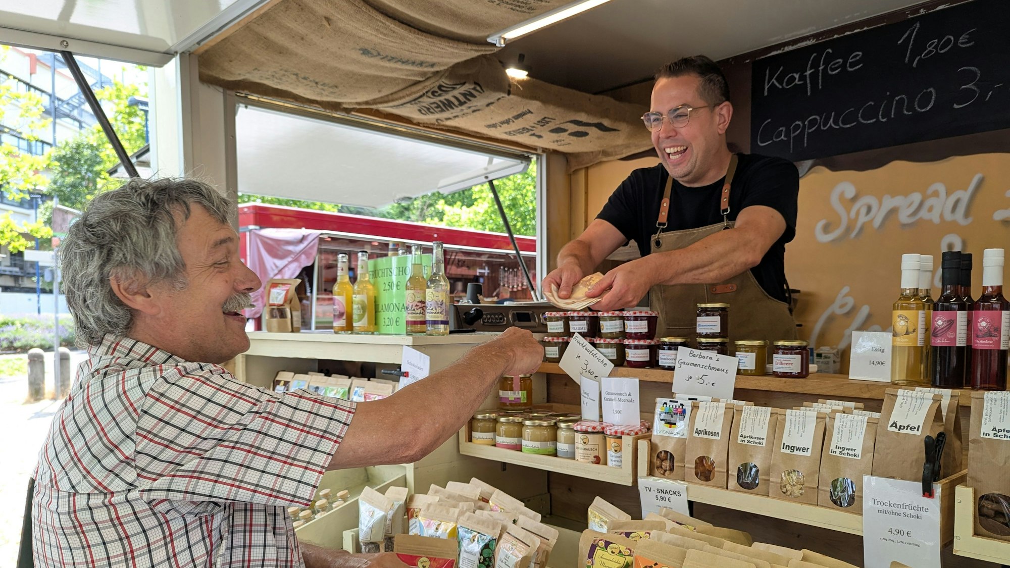Das Foto zeigt den Marktmeister und einen Händler an seinem Pralinen-Stand auf dem Hürther Wochenmarkt.