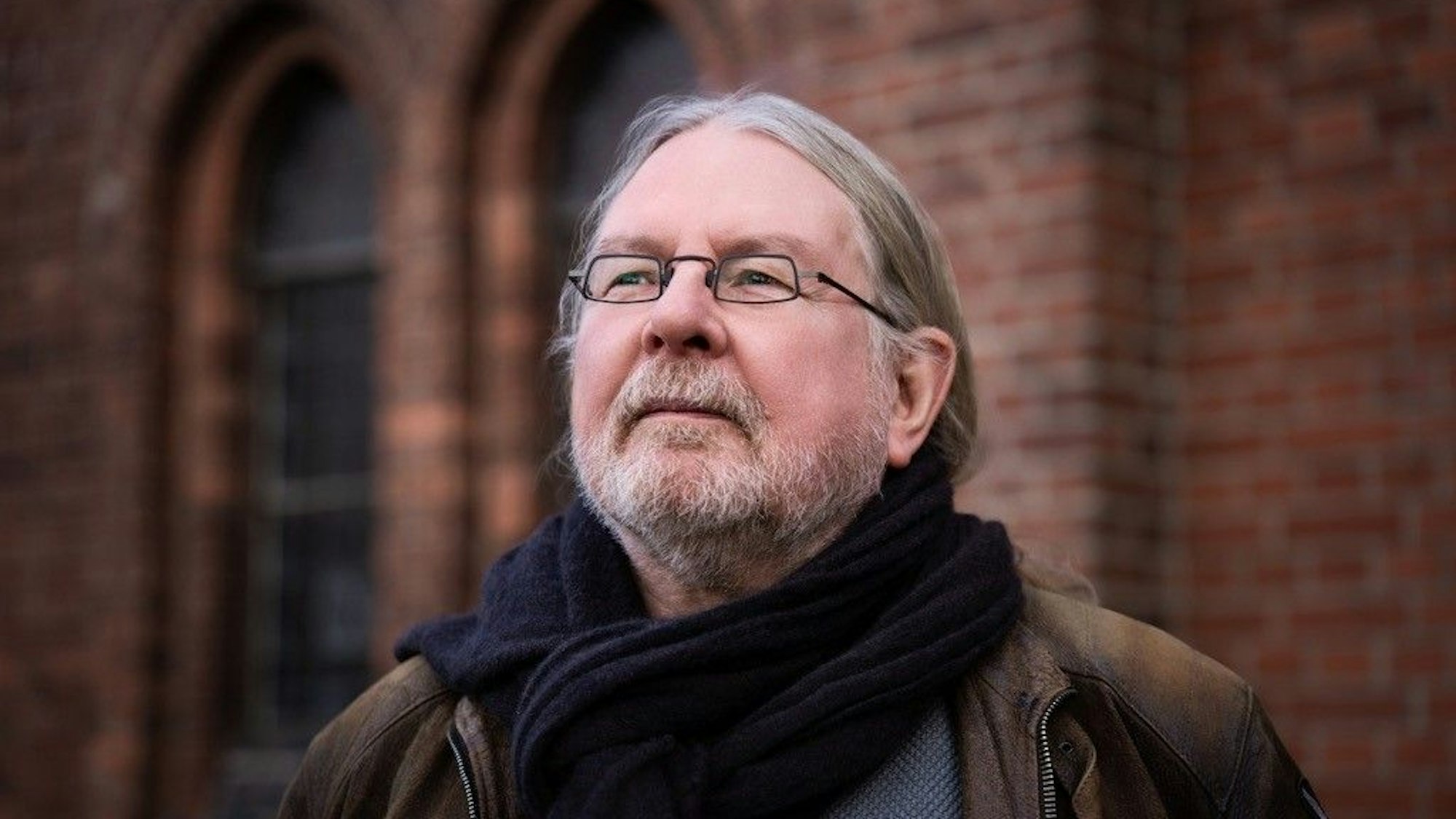 Herr Diederichs steht vor einer Backsteinfassade einer Kirche und schaut in die Weite.