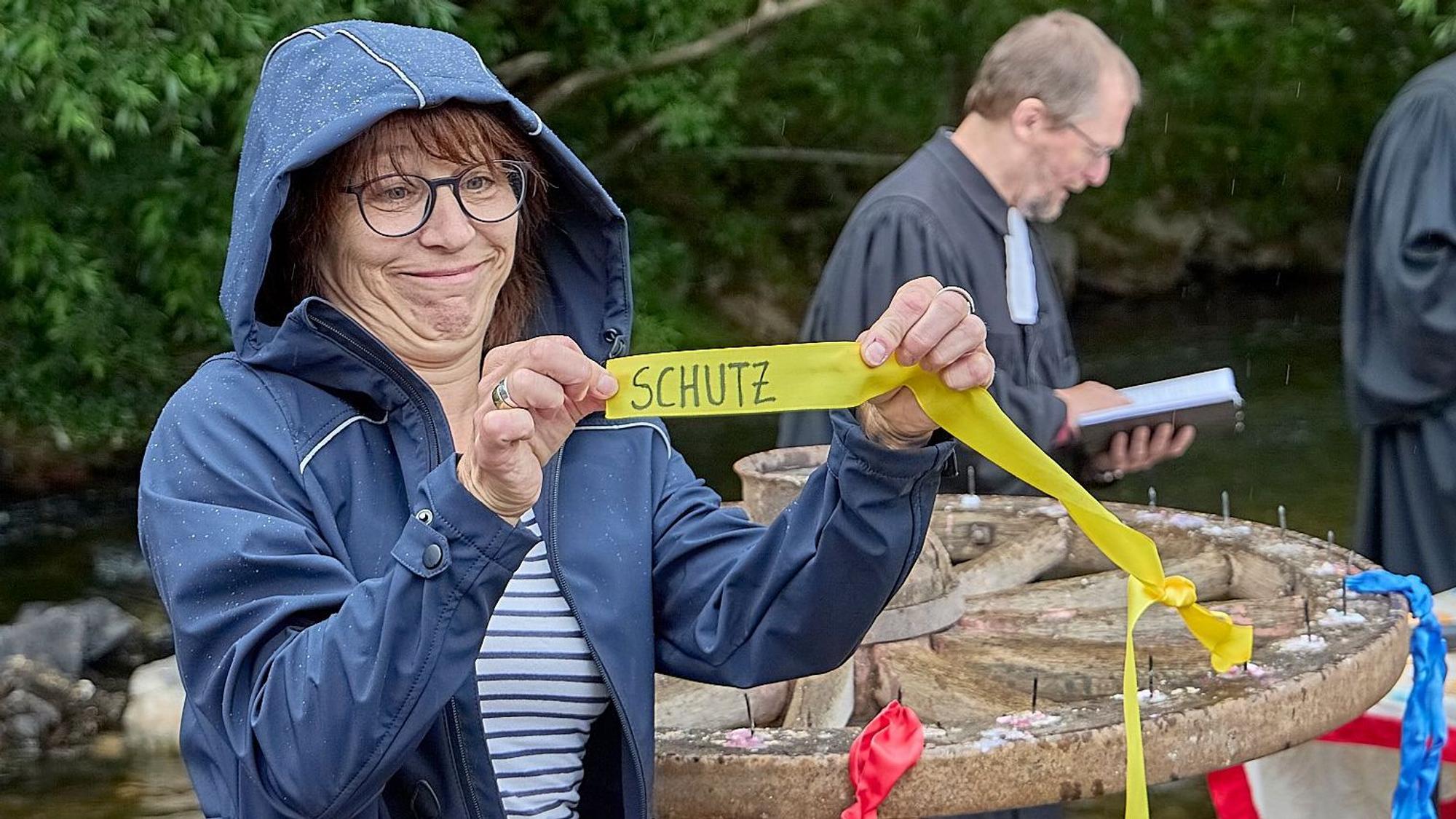 Eine Frau hält ein Band hoch, auf dem der Schriftzug „Schutz“ zu erkennen ist.