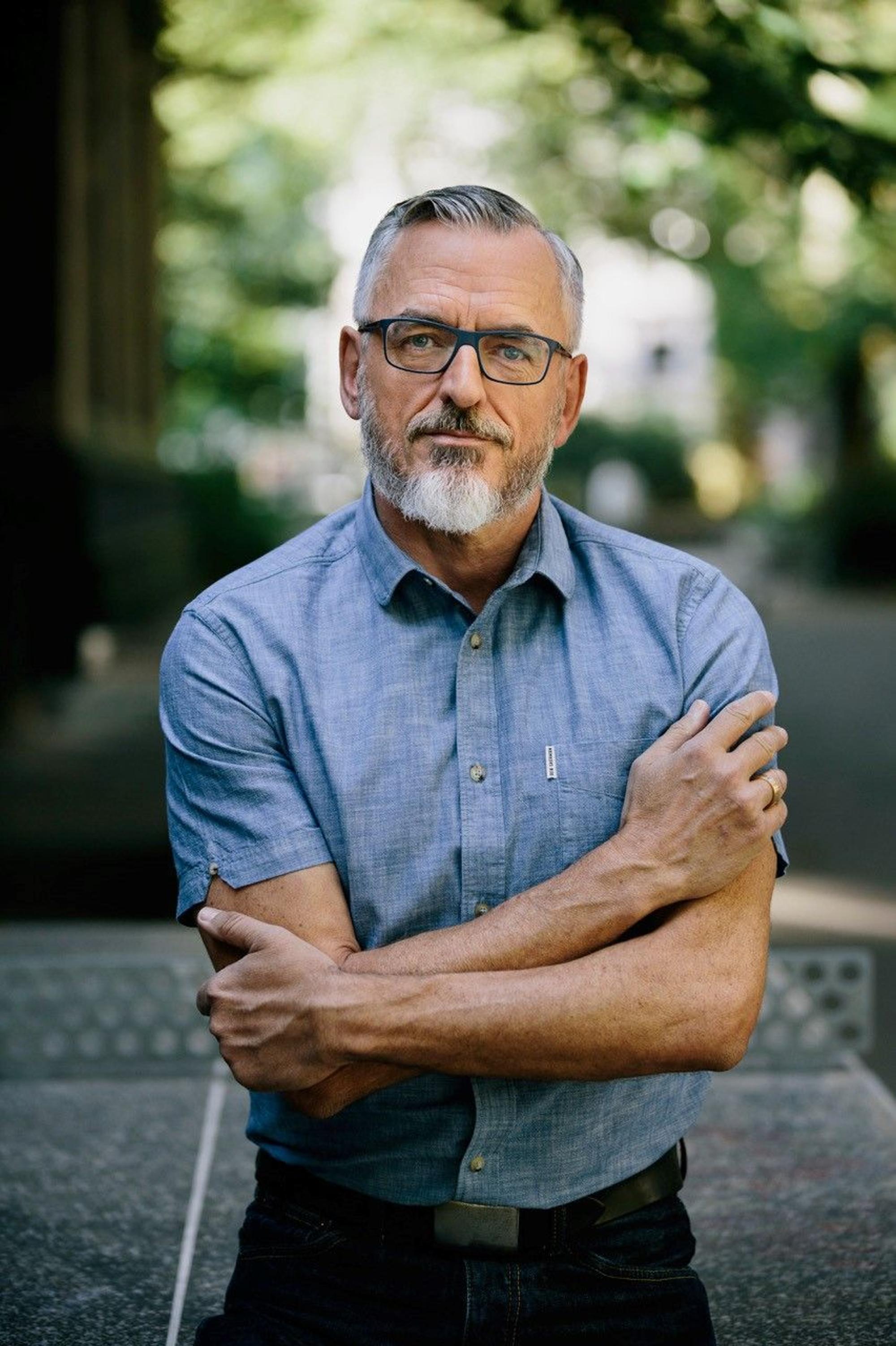 Frank Reifenberg trägt ein Kurzarmhemd in blau und schwarze Brille. Er ist im Halbporträt zu sehen.