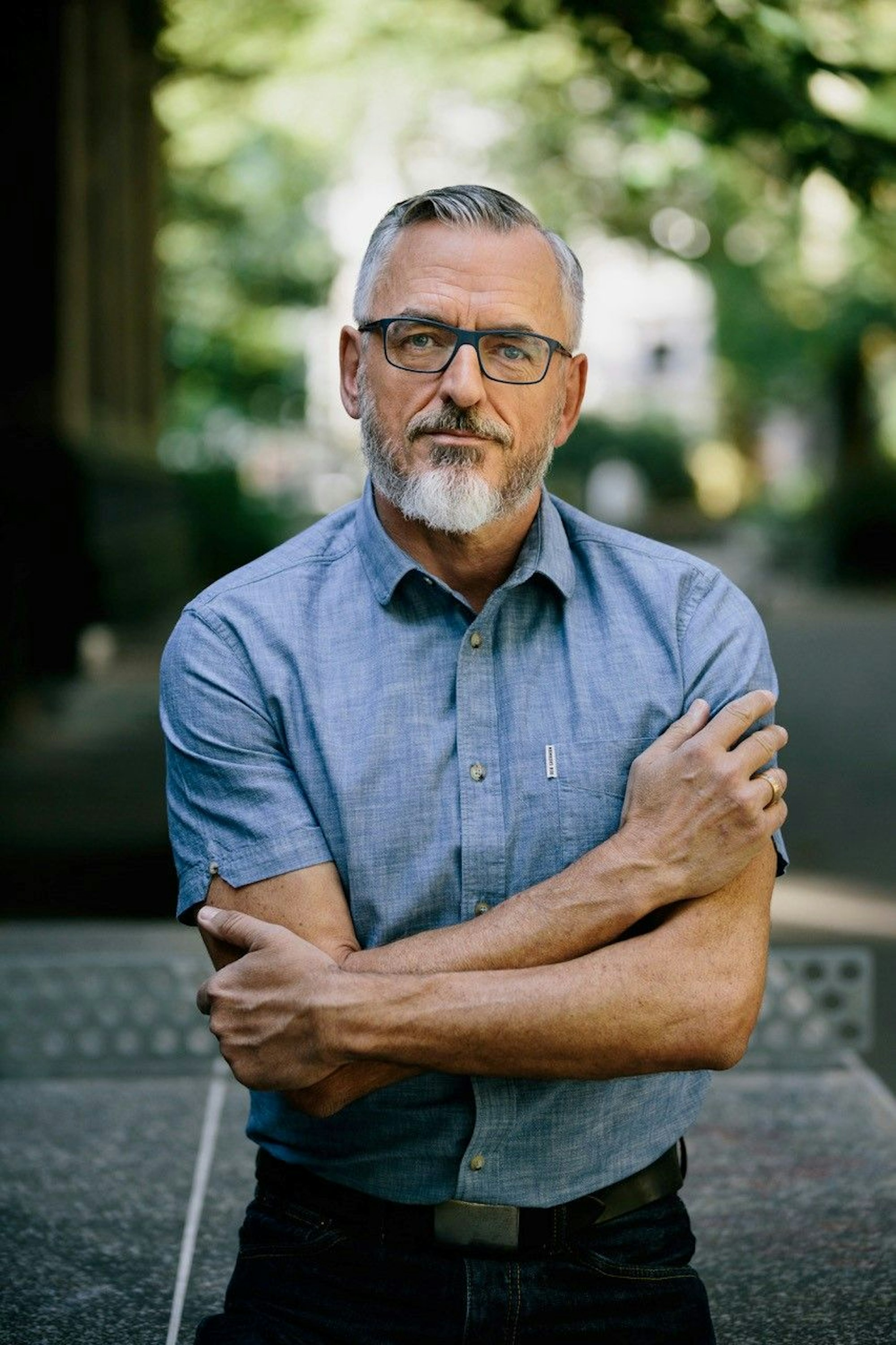 Frank Reifenberg trägt ein Kurzarmhemd in blau und schwarze Brille. Er ist im Halbporträt zu sehen.