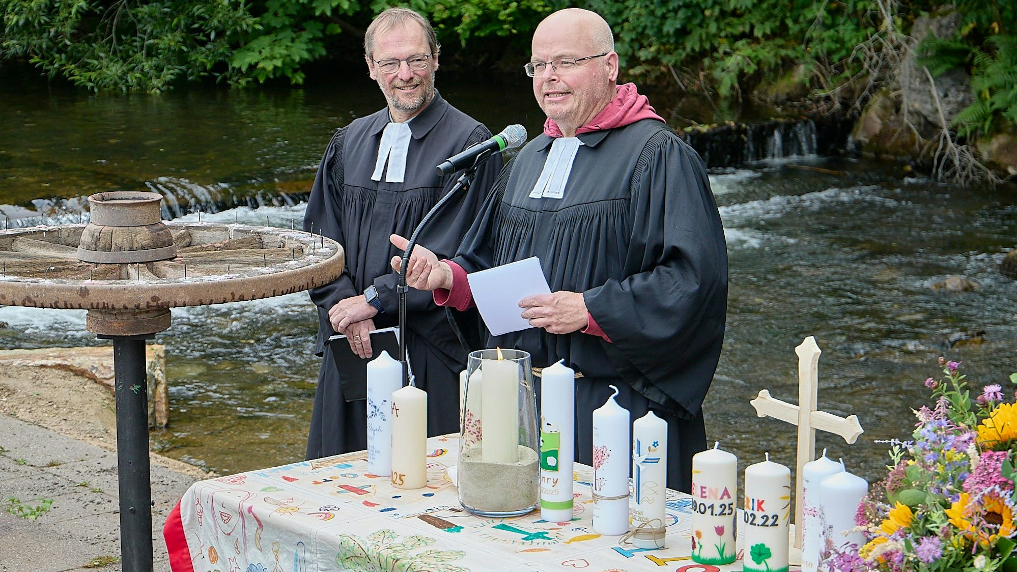 Die beiden Geistlichen stehen an einem Tisch, auf dem mehrere, mit Namen versehenen Kerzen aufgestellt worden sind.