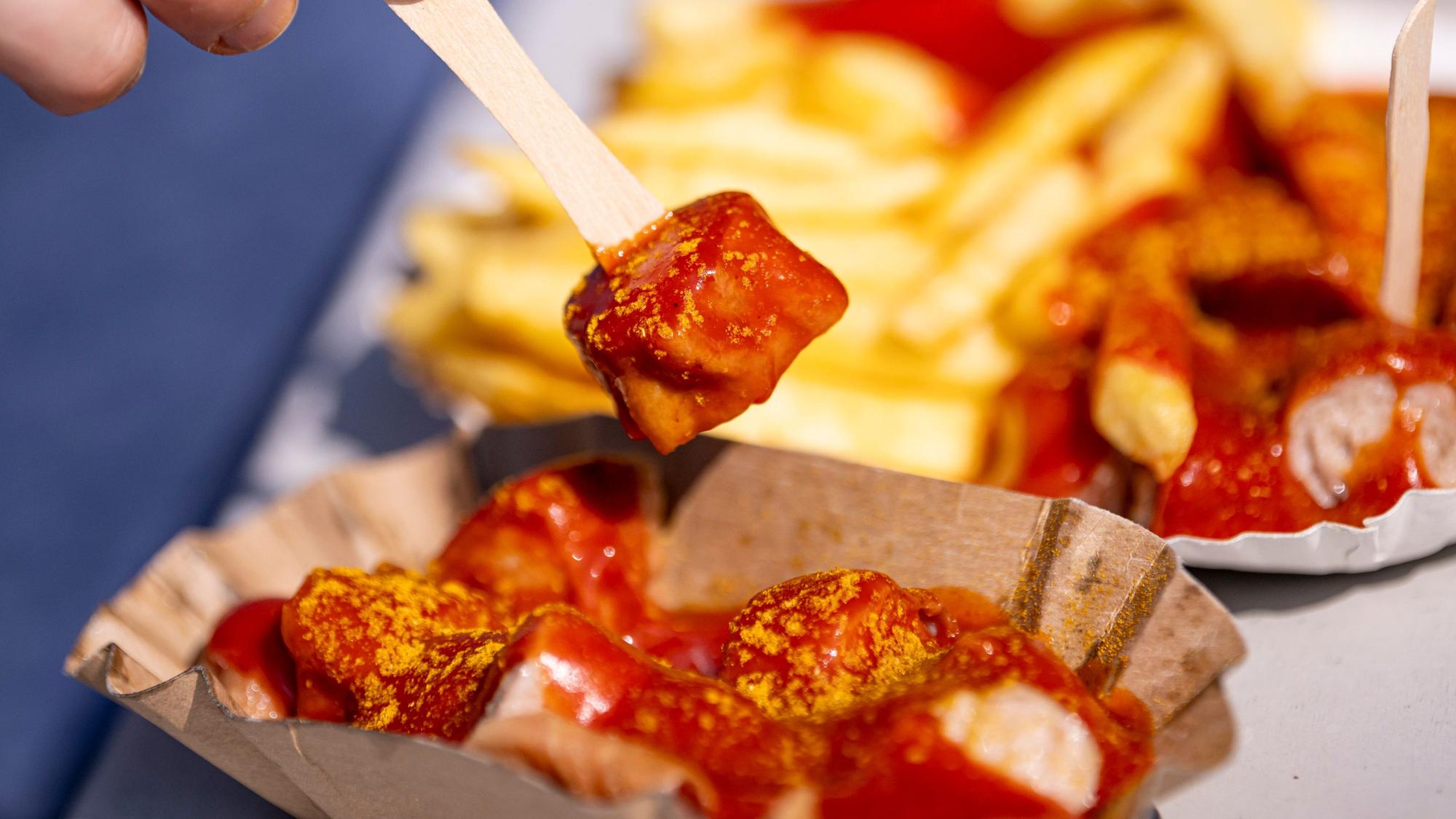 Eine Person spießt ein Stück Currywurst auf.