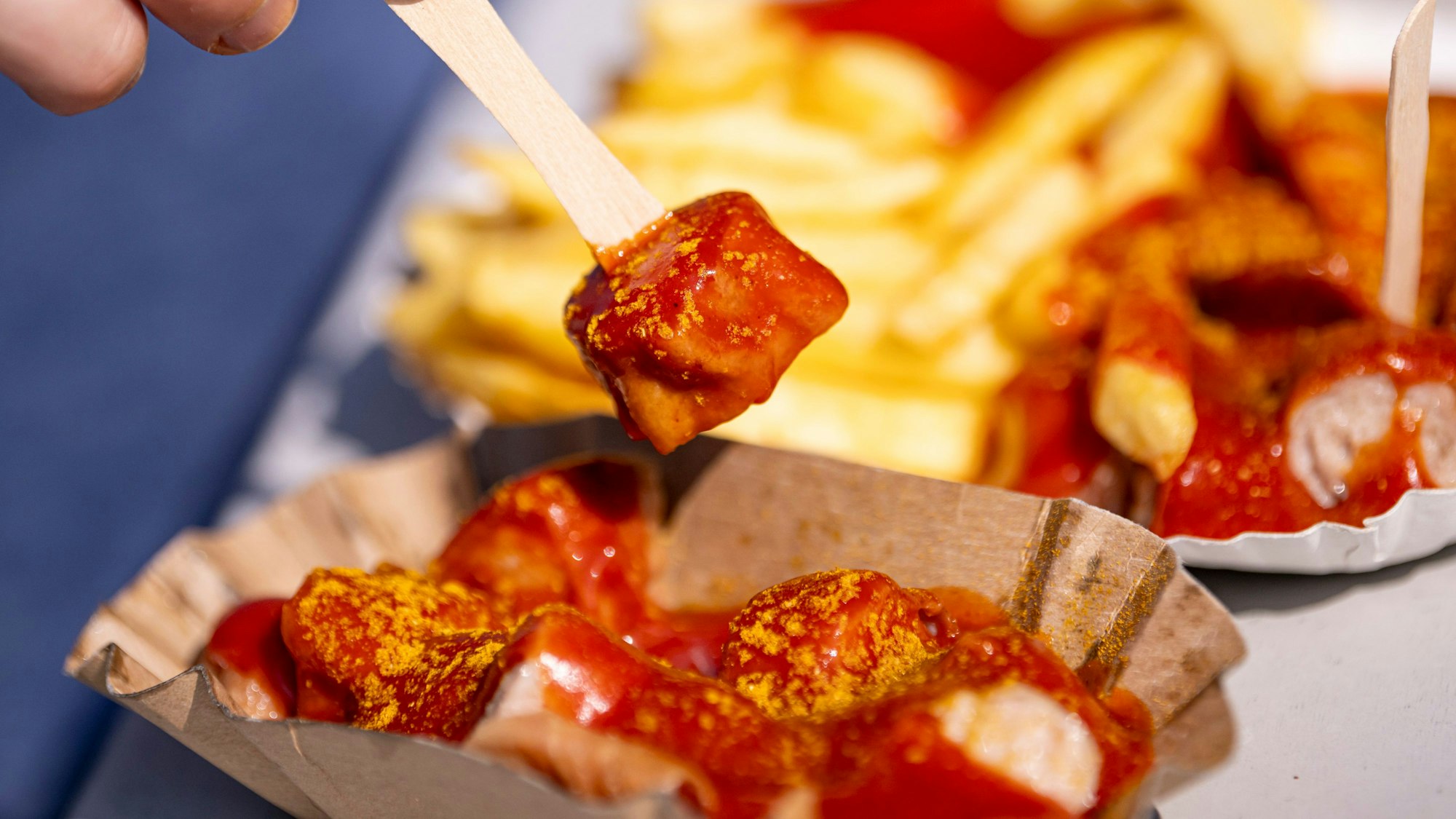 Eine Person spießt ein Stück Currywurst auf.