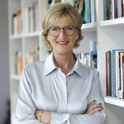 Christiane Woopen steht vor einem Bücherregal und lächelt in die Kamera.