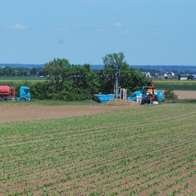 Das Bild zeigt ein Erdbohrgerät und einen Lastwagen am Rand eines Ackers.