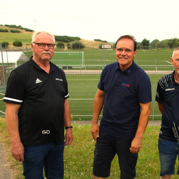 Vier Männer stehen vor einem Fußballplatz.