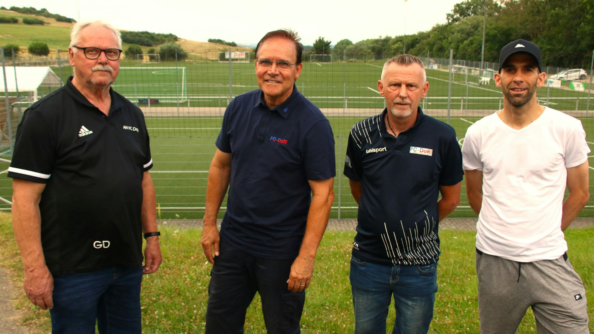 Vier Männer stehen vor einem Fußballplatz.