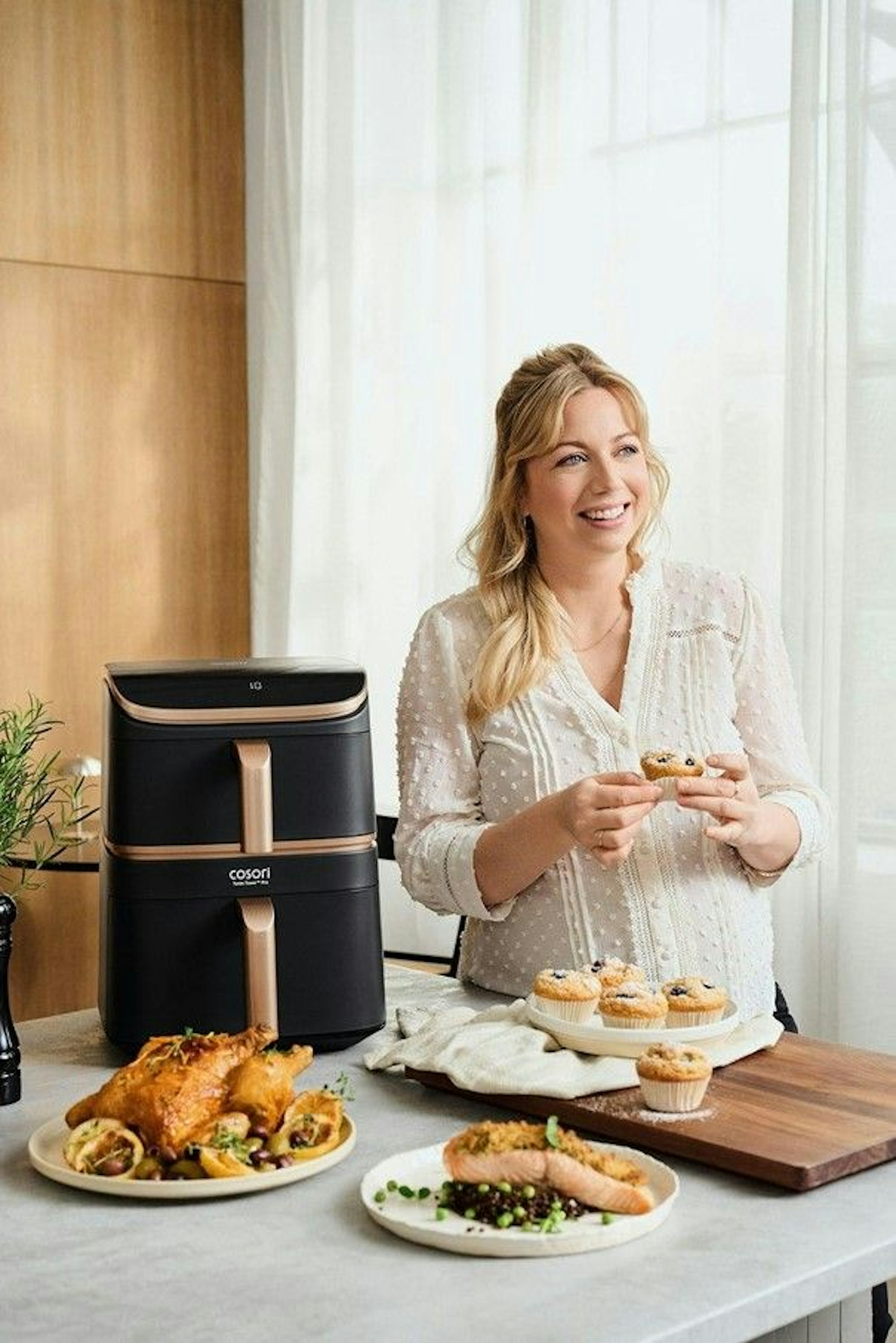 Zora Klipp neben dem COSORI Turbo Tower Pro Smart, umgeben von gekochtem Essen und Muffins.