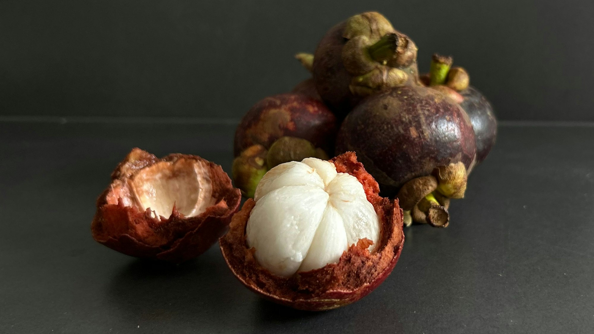 Von außen dunkelviolett und dickschalig, überrascht sie innen mit zartem, weißen Fruchtfleisch, das in Segmente geteilt ist, erinnert an Knoblauchzehen.