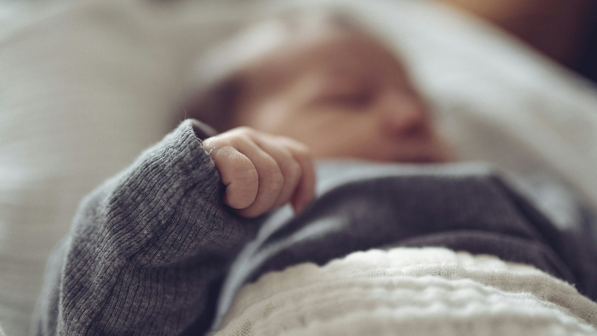 Schlafendes Baby in einem grauen Pullover, eingehüllt in eine weiche Decke. (Archivbild)