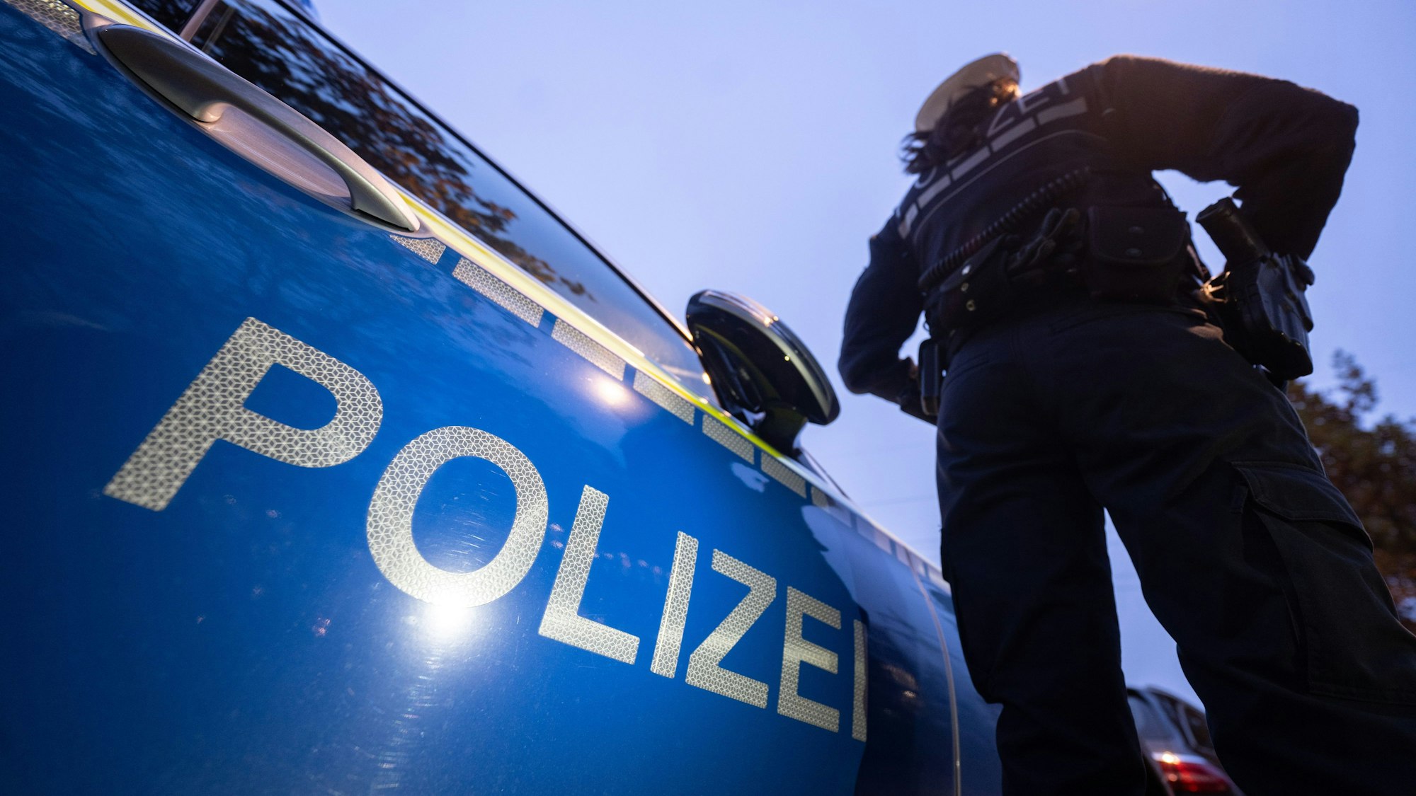 Eine Polizistin steht neben einem Polizeifahrzeug.