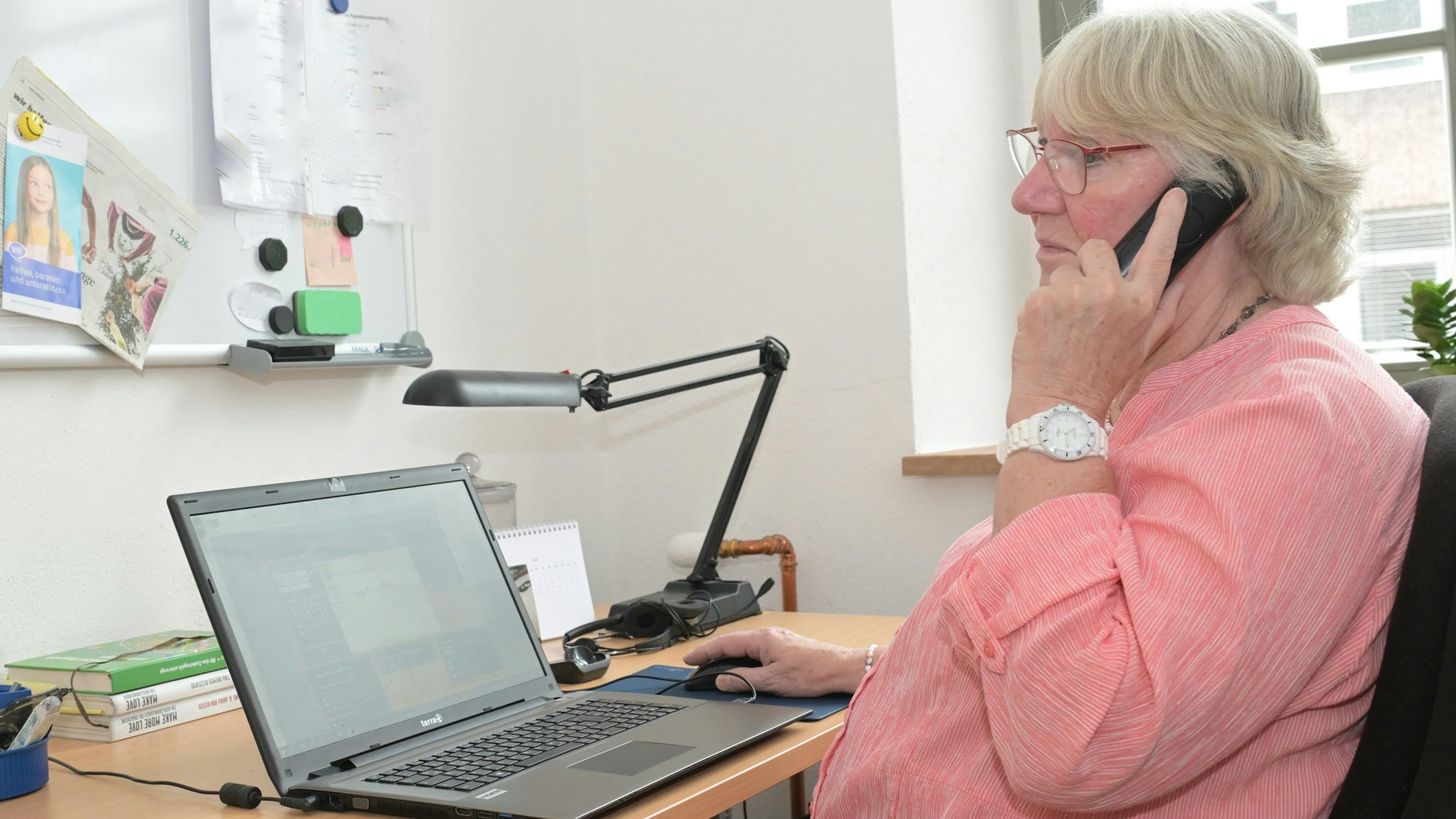Eine Frau sitzt vor einem Laptop und hält einen Telefonhörer ans Ohr.