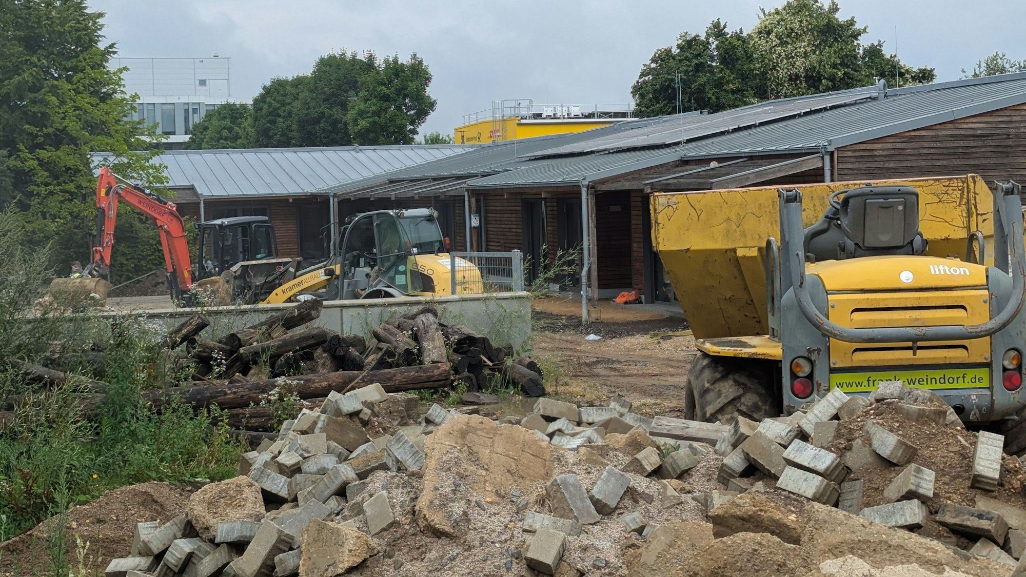 Das Foto zeigt Baufahrzeuge und Bauschutt vor dem Holzgebäude der Kita in Kalscheuren.