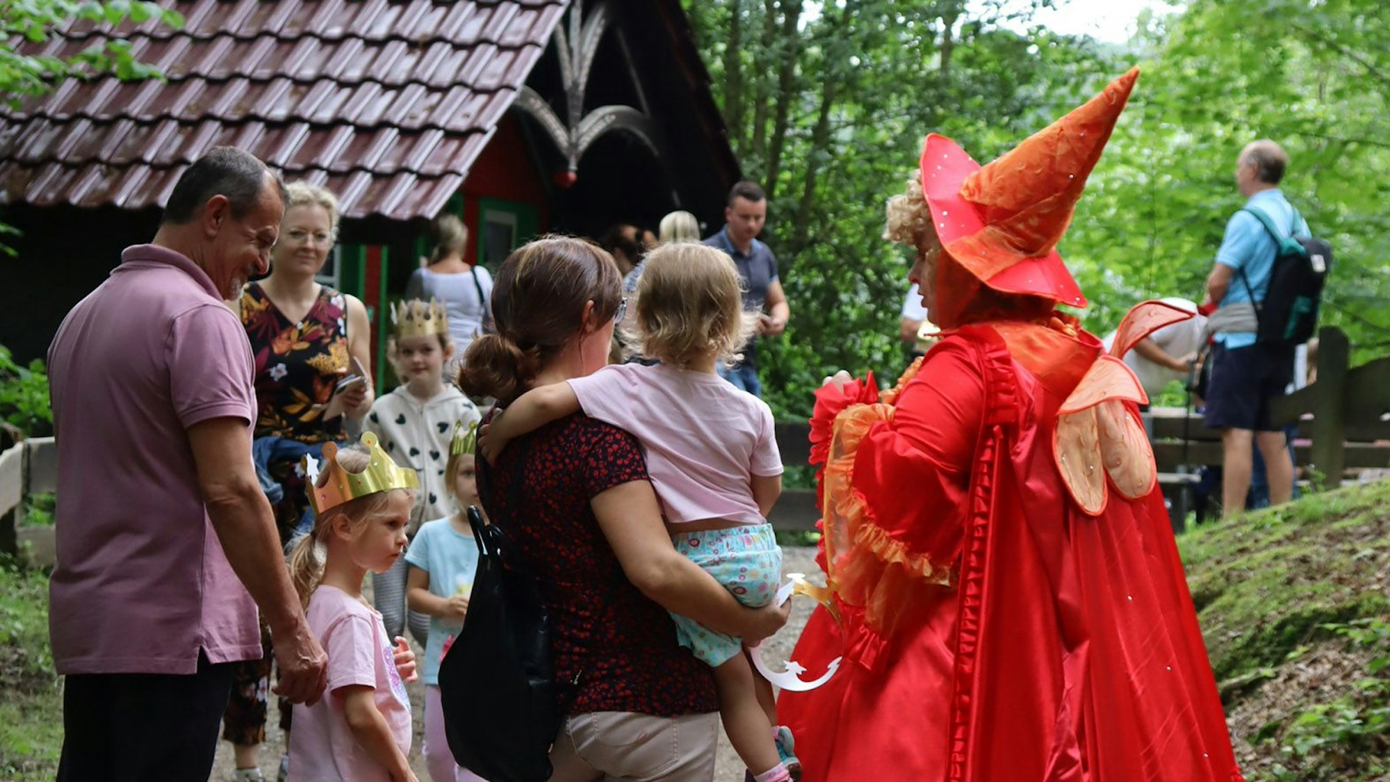 Besuchende im Altenberger Märchenwald, Mehrere Familien mit Kindern sind zu sehen, dazu eine Frau in rotem Feenkostüm.