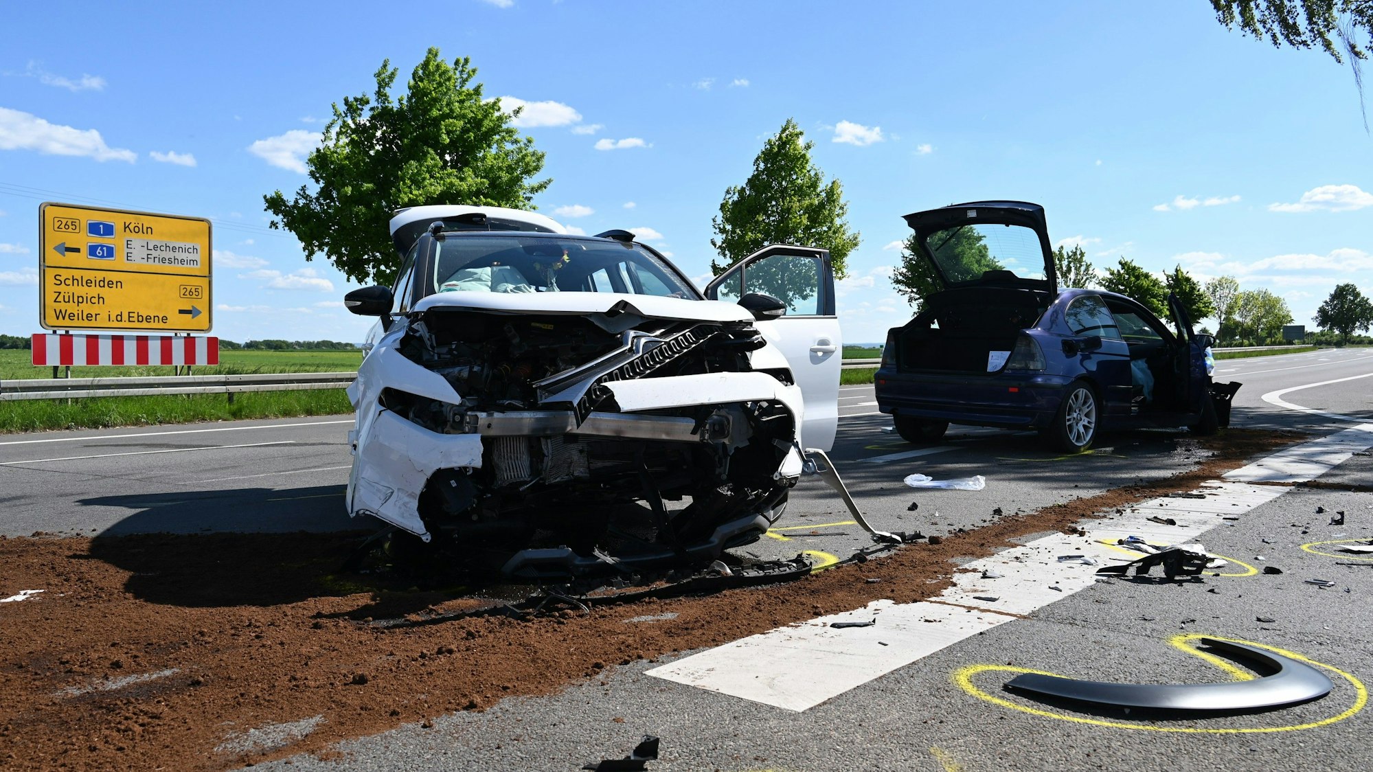 Zu sehen sind zwei Autos nach einem Unfall auf einer Kreuzung, im Hintergrund steht ein Krankenwagen.