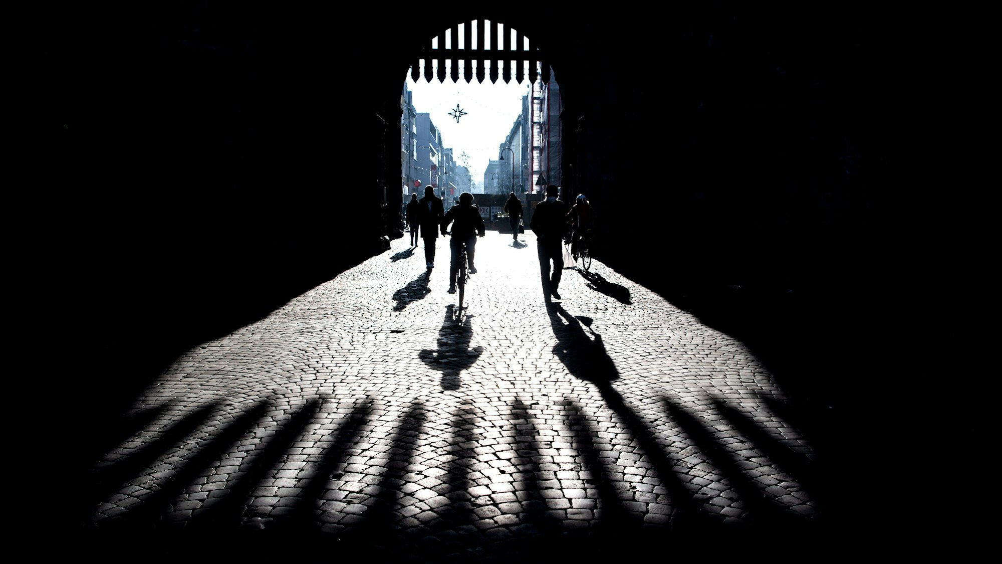Passanten werfen Schatten auf das Pflaster bei der Eigelstein Torburg.